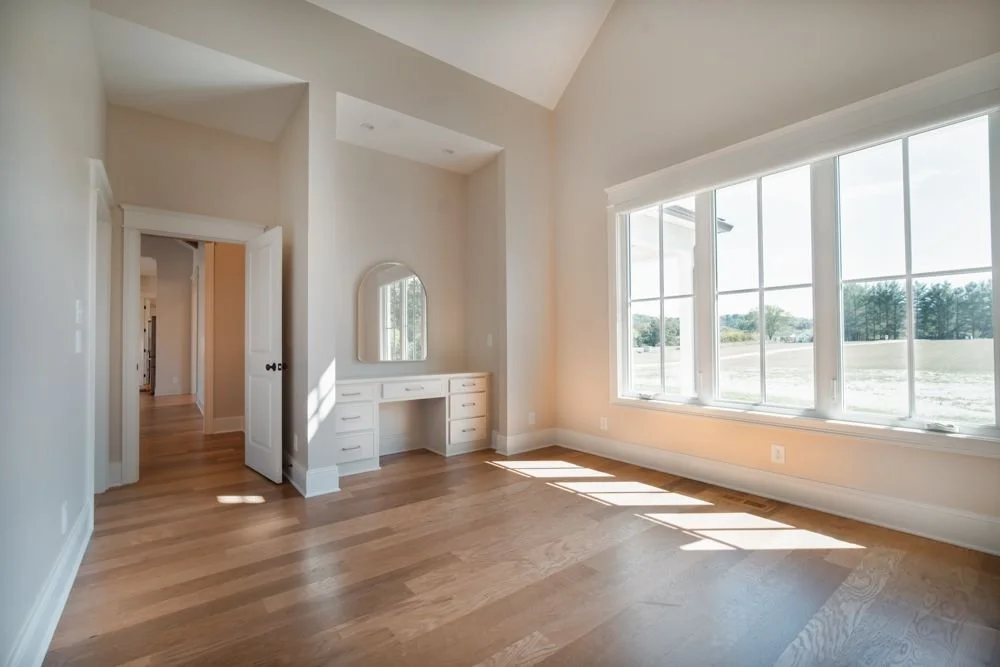 Bright room with a wall of windows, wood floors and a built-in vanity desk with an arched mirror