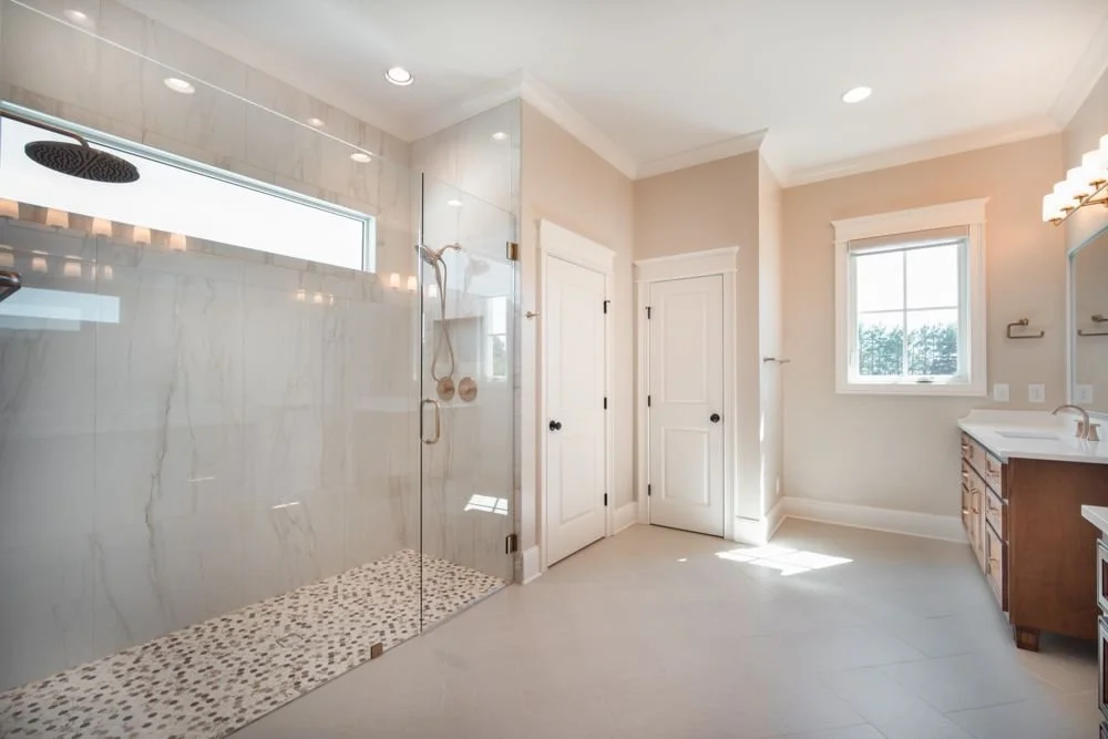 Bathroom with a large glass walk-in shower, pebble shower floor and a wood vanity