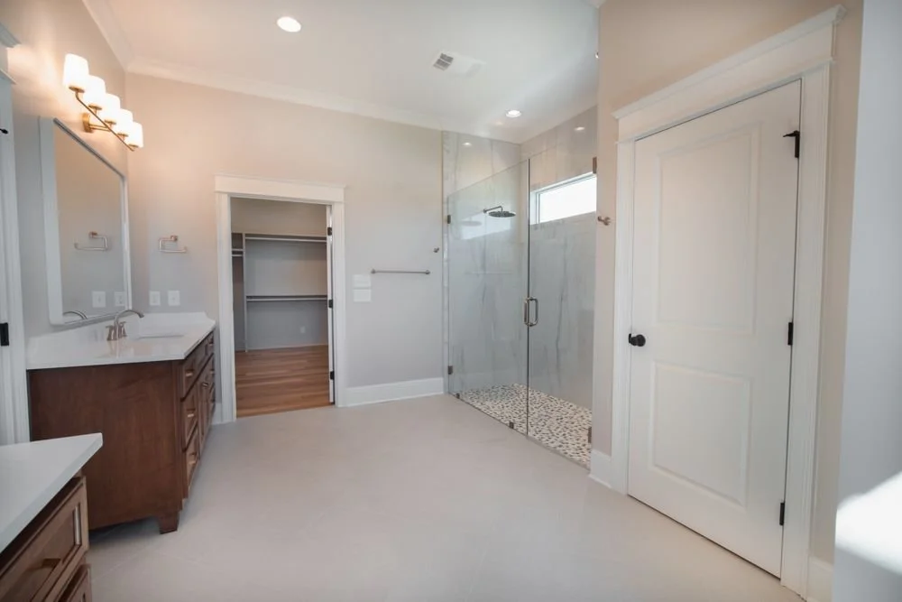 Bathroom with a wood vanity, glass shower and a doorway into a walk-in closet