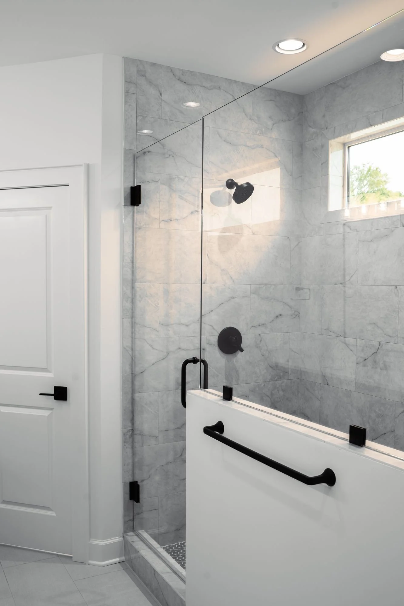 Glass shower with gray veined tile walls and black fixtures and grab bar (portrait)