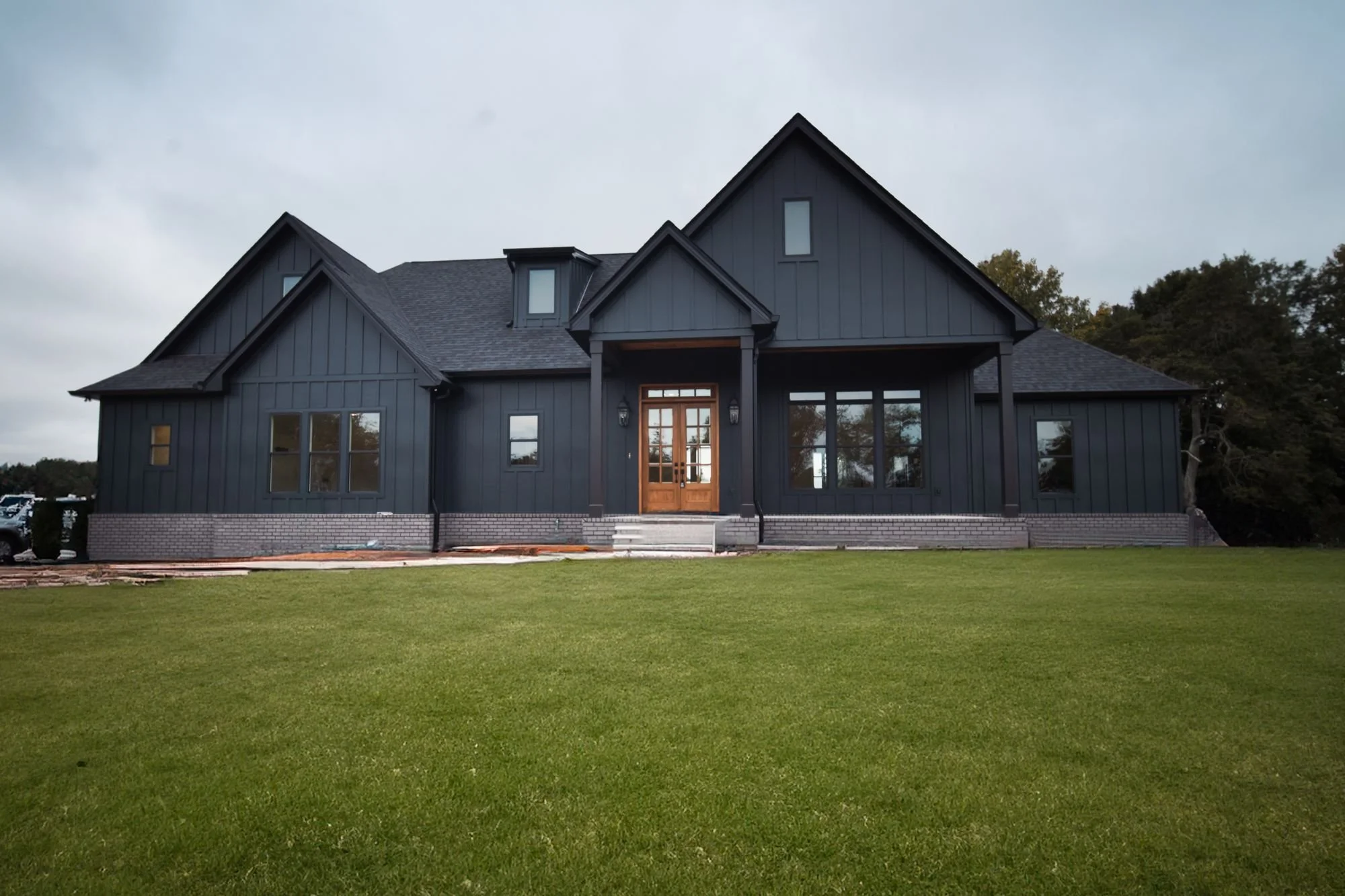 Front of a dark custom home in Lebanon, TN with vertical siding, a gabled roof, a covered entry and wood and glass double front doors