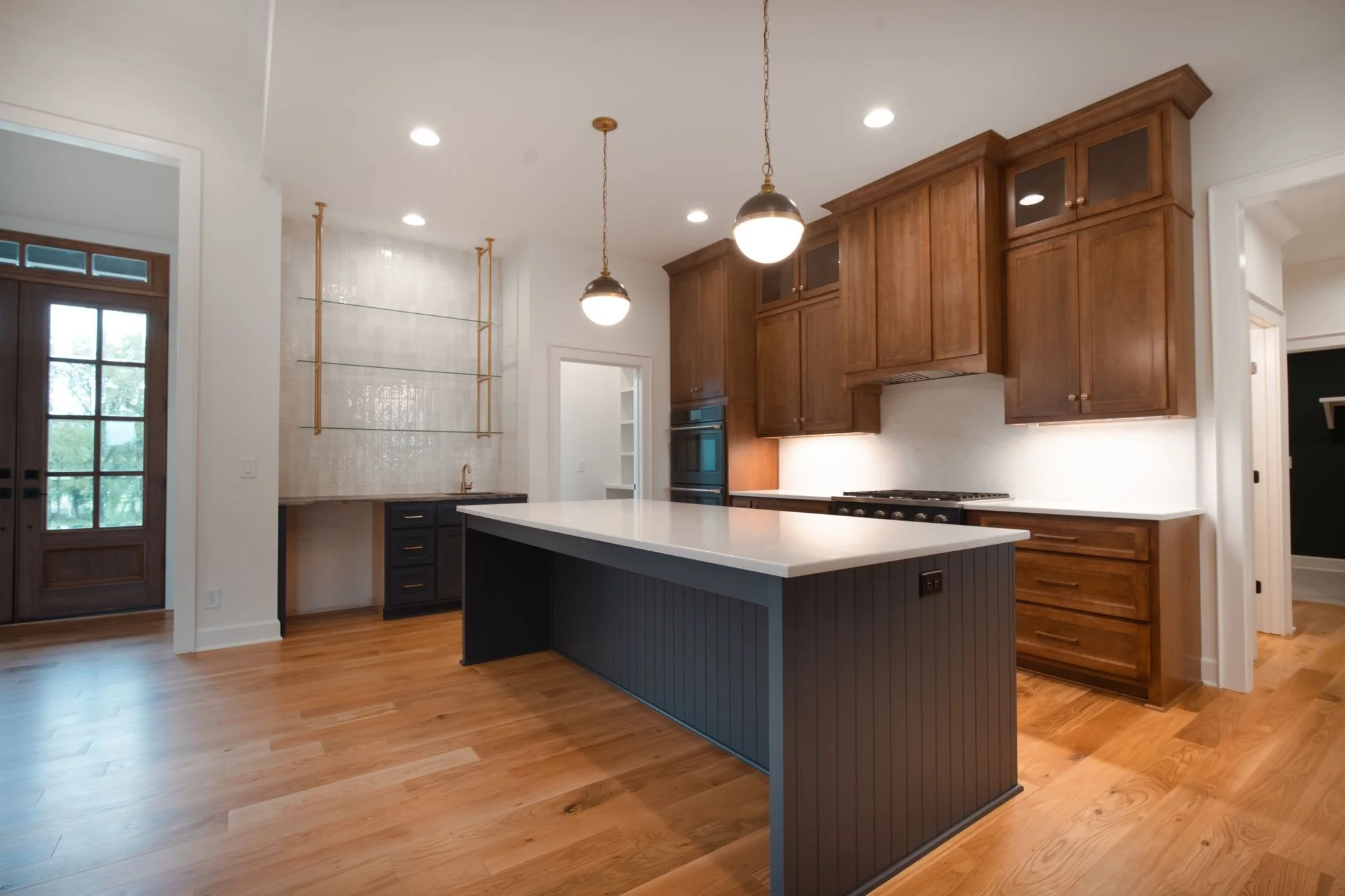 Kitchen with a navy island, stained wood upper cabinets, globe pendant lights and brass open shelving