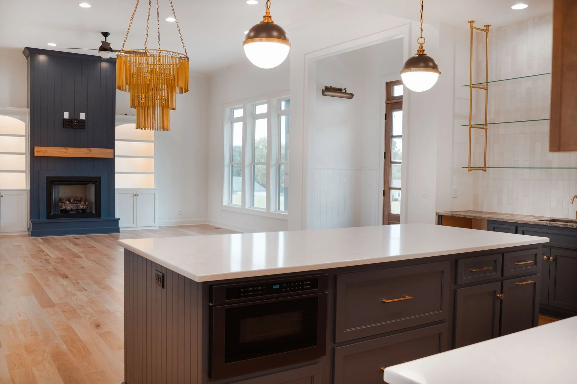 Navy kitchen island with a built-in microwave drawer, open to a living room with a navy fireplace wall and a gold chandelier