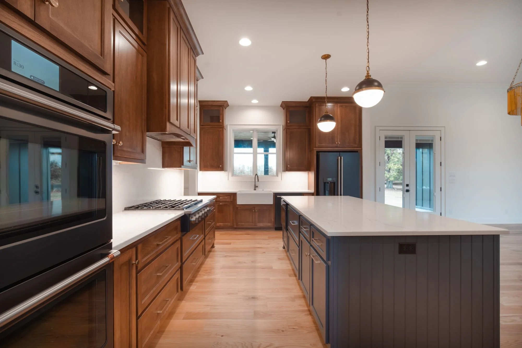 Galley view of stained wood cabinets with double wall ovens, a gas cooktop and a navy island