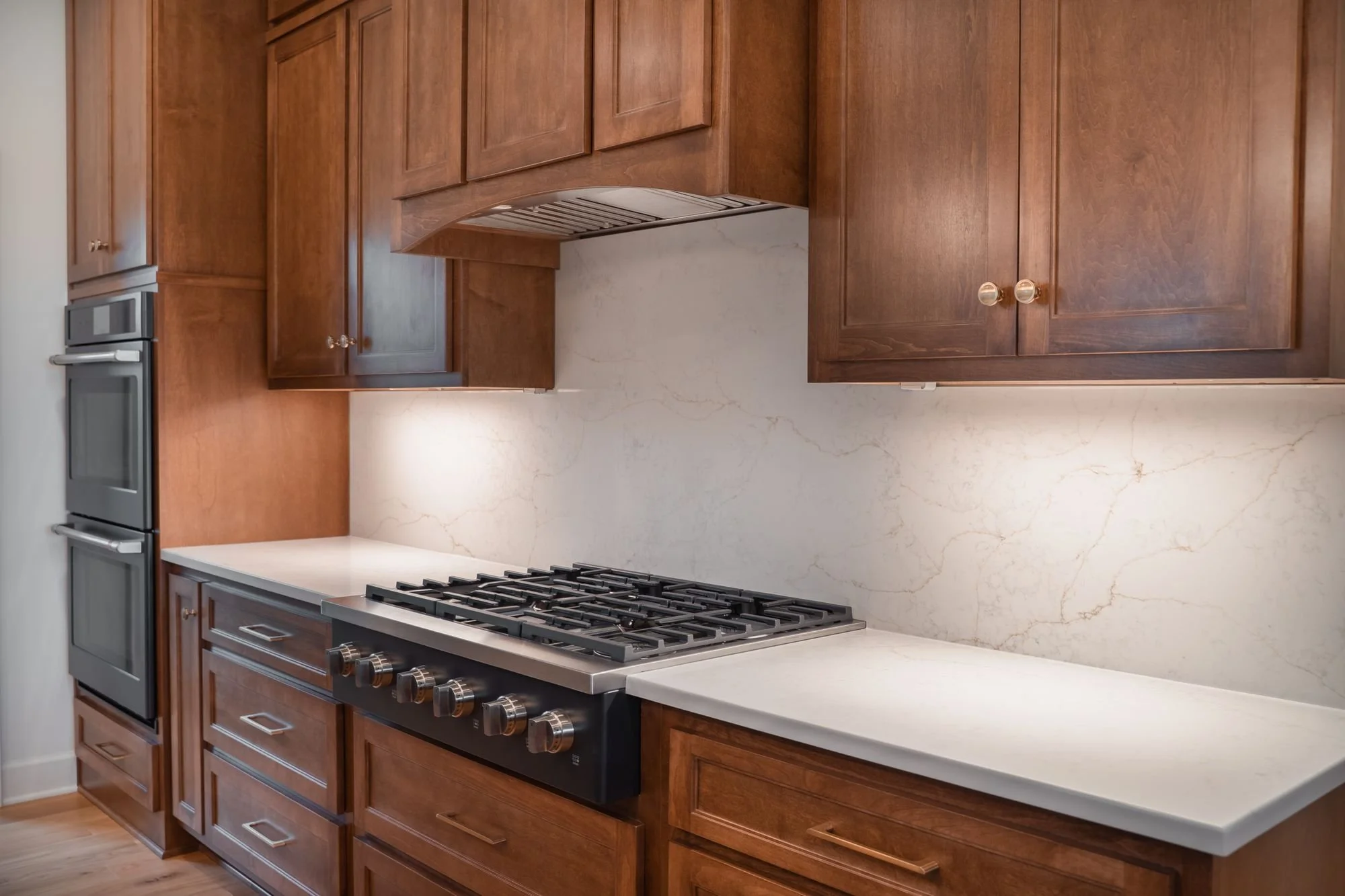 Gas cooktop set into stained wood cabinets with white countertops and a white stone backsplash