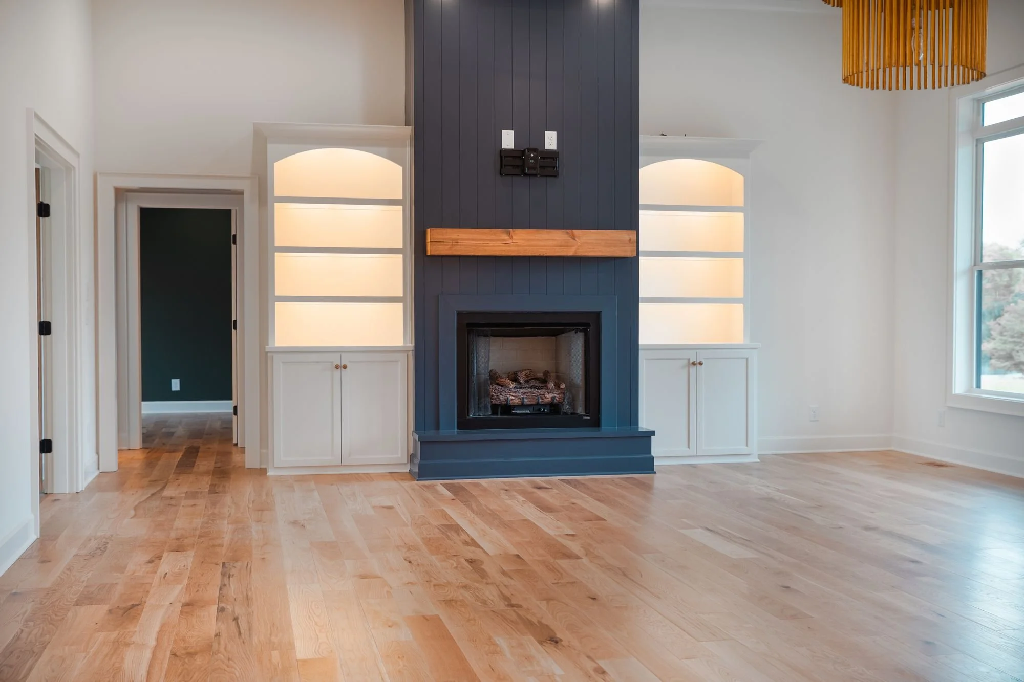 Living room with a navy fireplace wall, wood mantel and lit arched built-in shelves on both sides