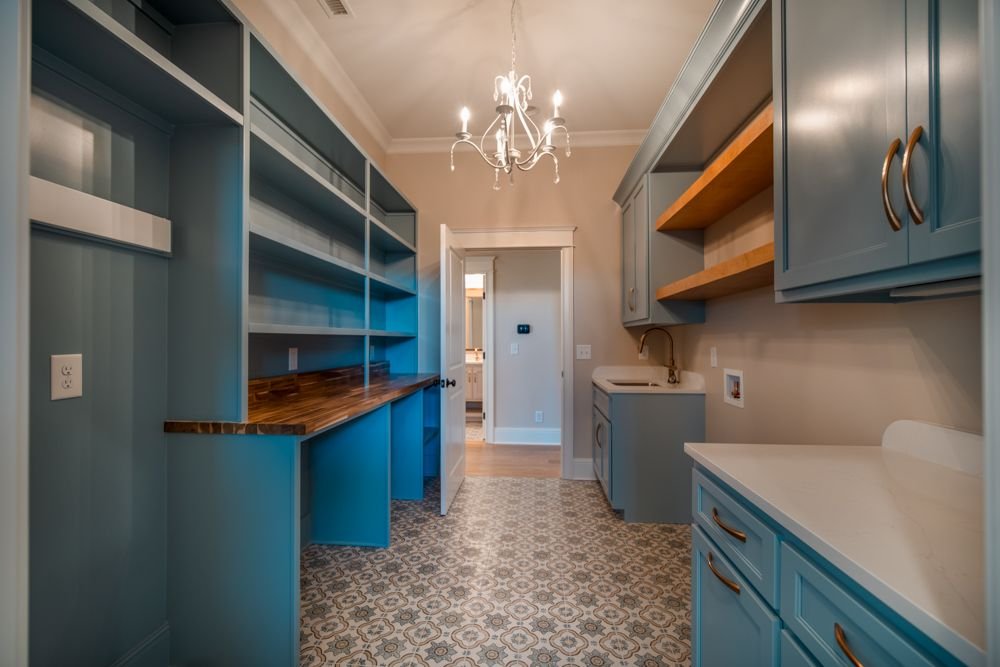 Room with blue built-in cabinets, open wood shelves, patterned tile floor and a chandelier
