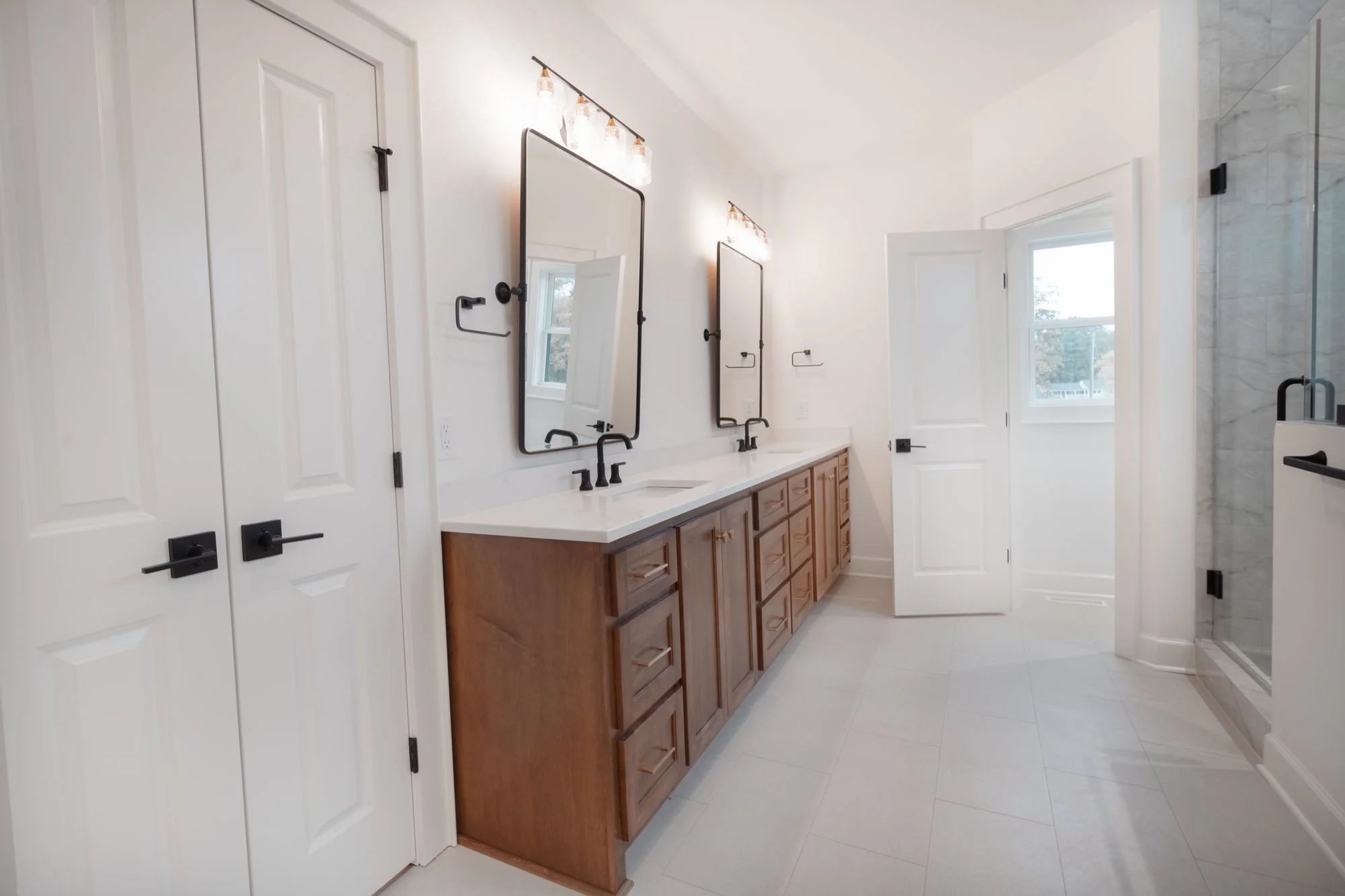 Bathroom with a wood double vanity, black mirrors and fixtures and a glass shower
