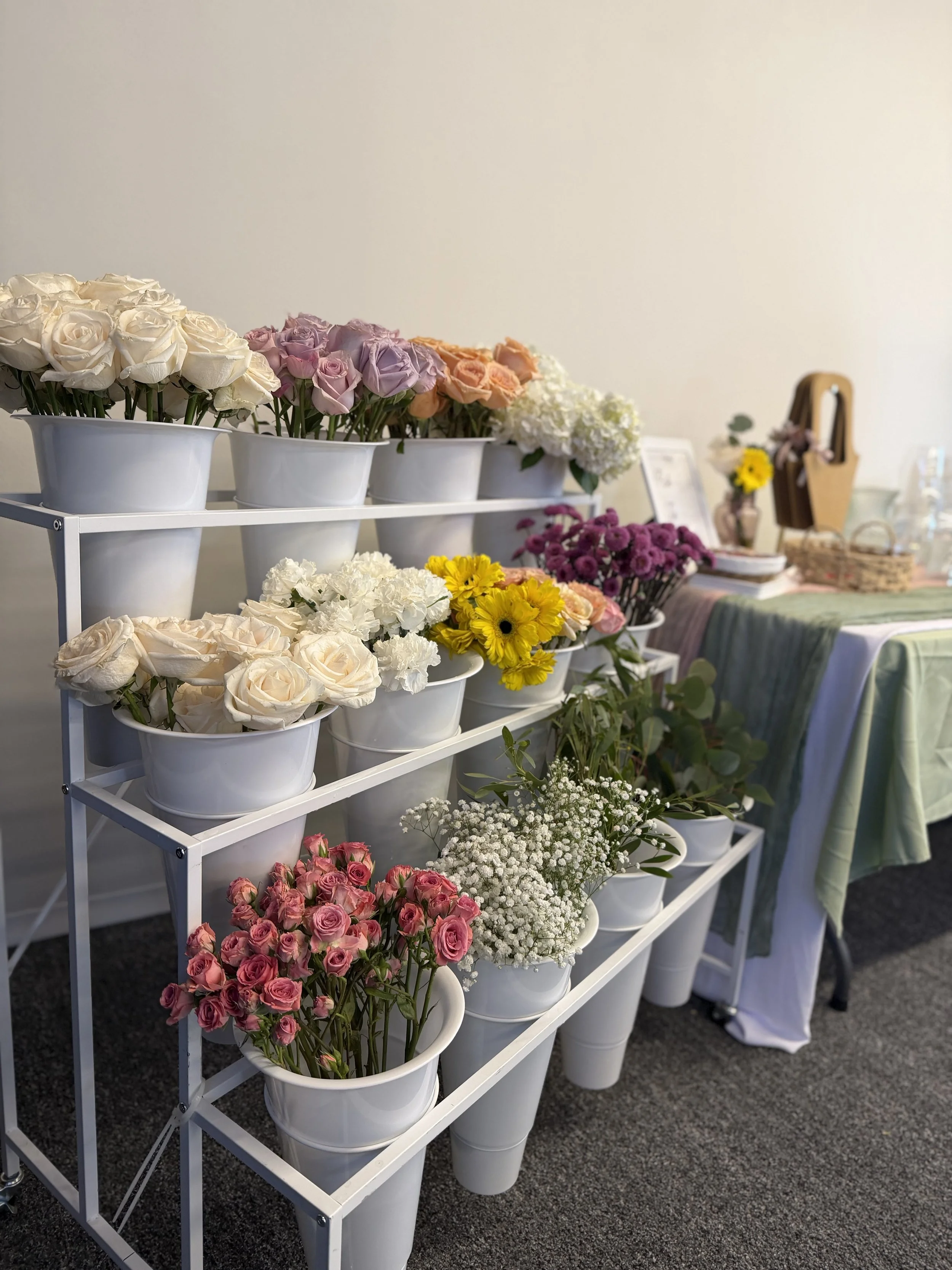 Tiered white shelves of fresh flower buckets at an indoor Colorado bloom bar