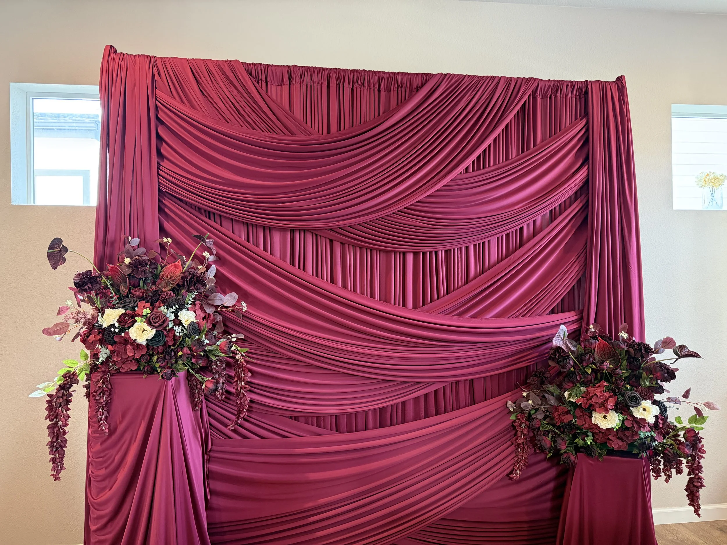 A wedding backdrop with pink draped fabric and floral arrangements.