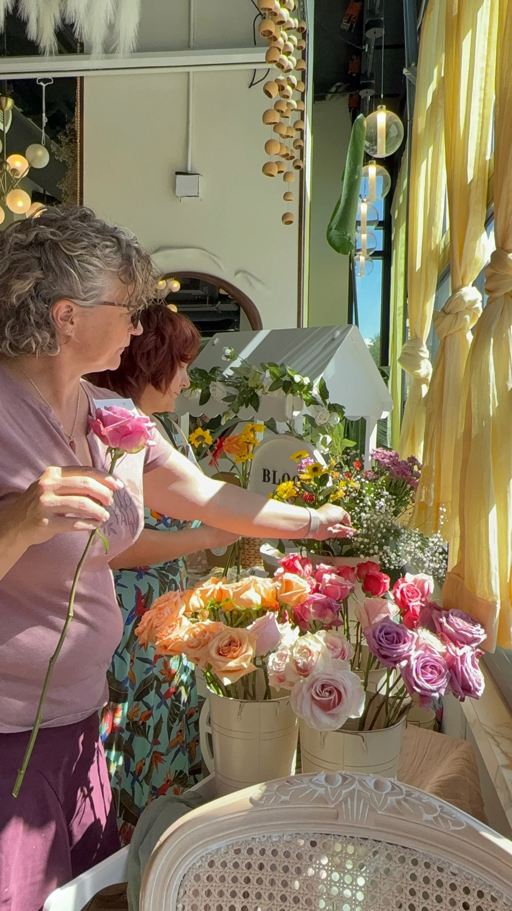 The same guest examining a single stem, buckets of coral roses beside her.