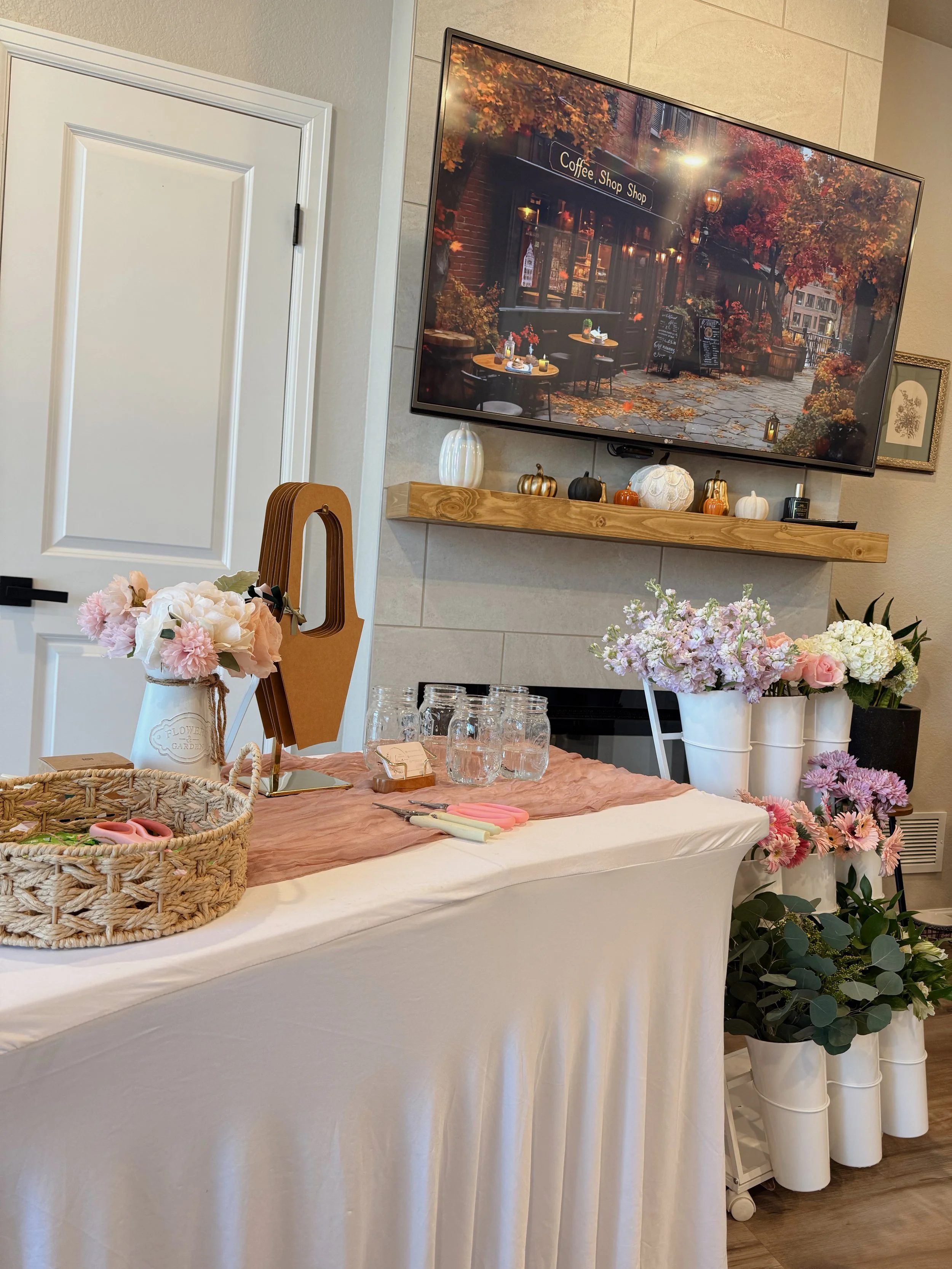 A cozy indoor bloom bar featuring baskets, bud vases, and curated faux florals arranged on a soft neutral table covering. Perfect for workshops, intimate events, and hands‑on floral experiences.