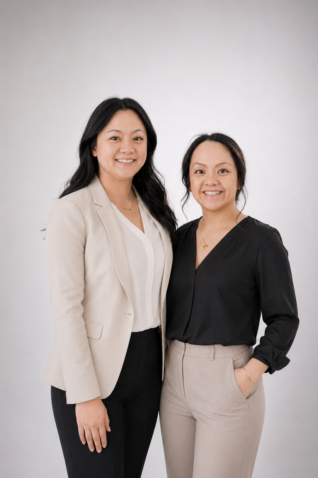 Two women standing close together, smiling, and wearing business casual attire against a plain white background.