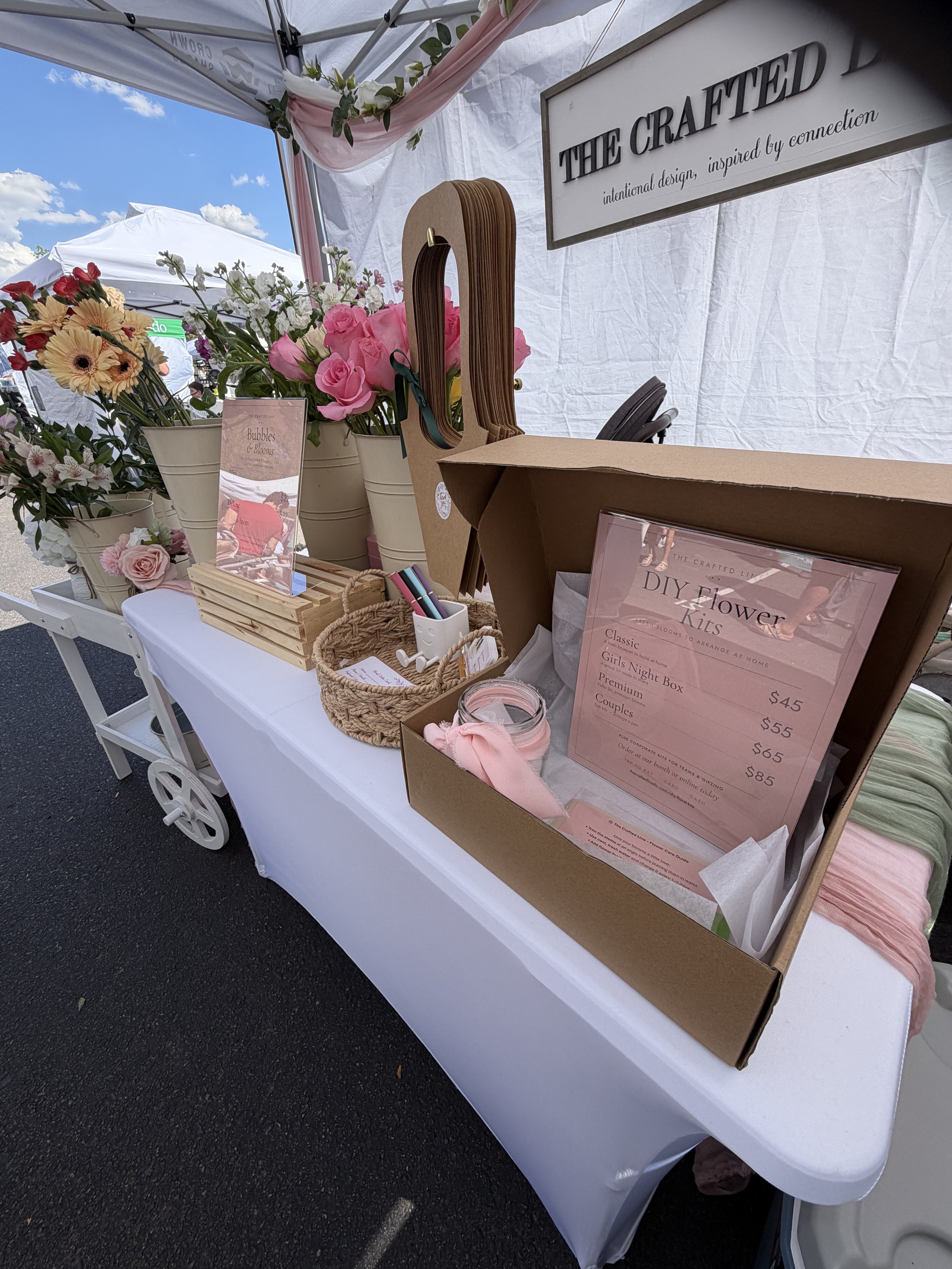 A wide shot of your vendor booth featuring pastel stationery, florals, and décor — showcasing your signature soft, curated market look.
