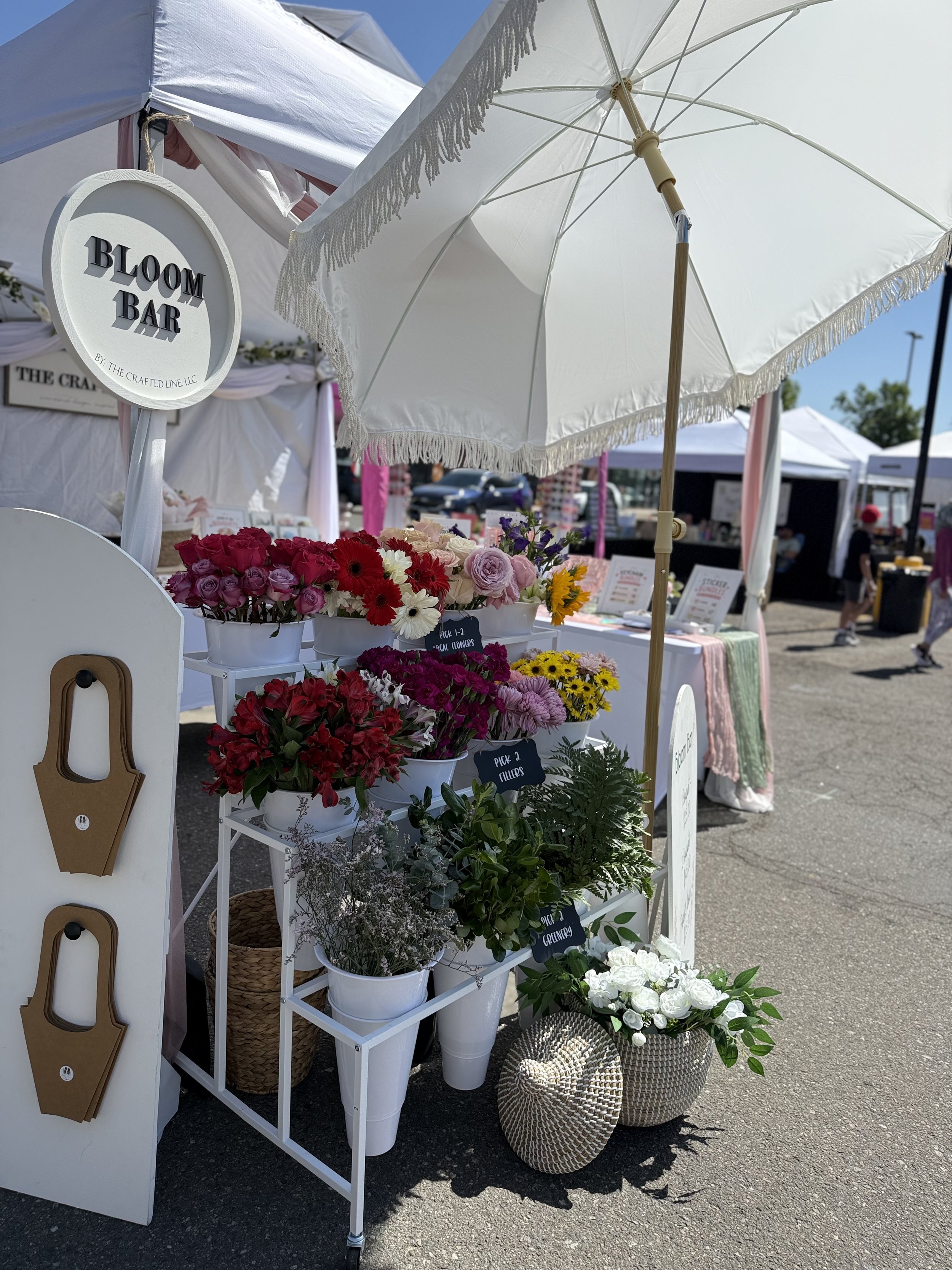 Bloom bar booth with round sign and rows of fresh stems at a Colorado market