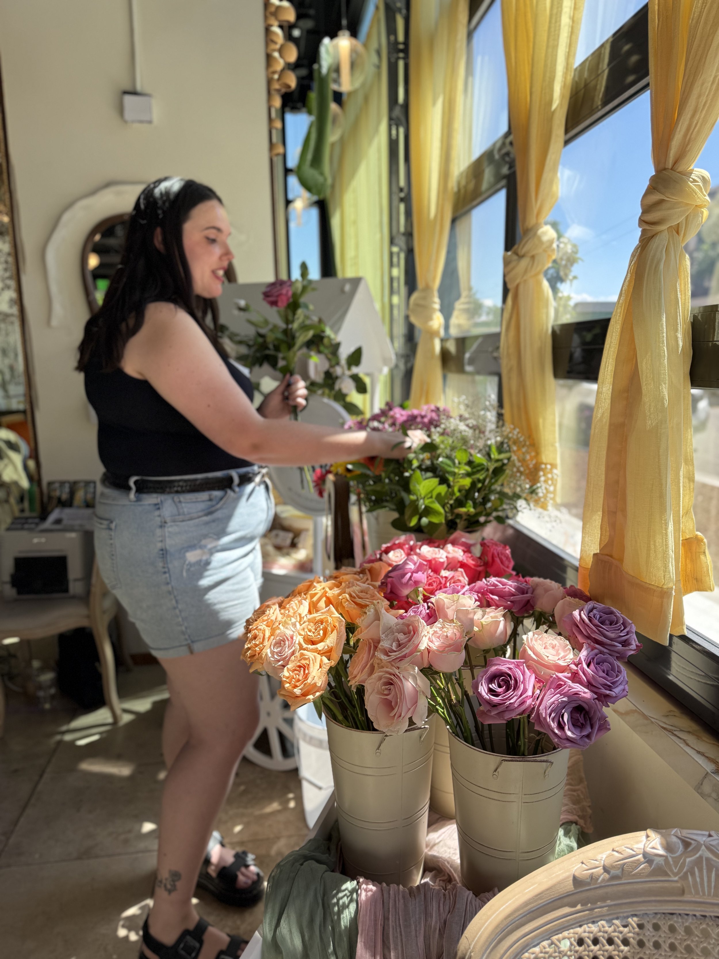 A guest in a black top and denim skirt adding a stem to her bouquet, buckets of blooms in the foreground.