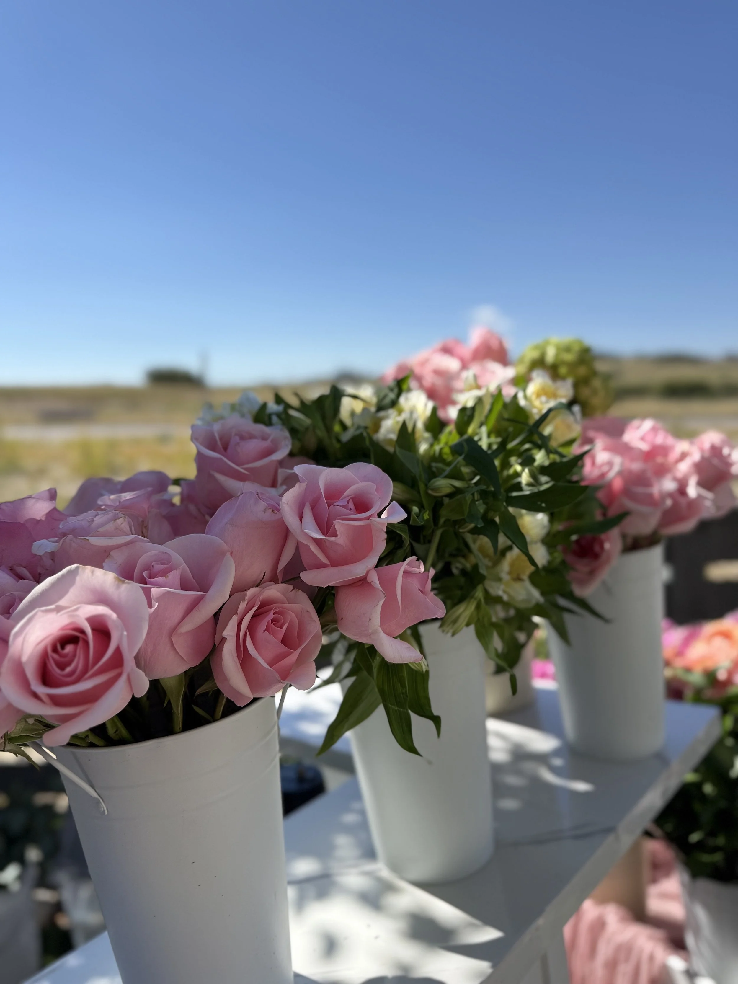 A collection of outdoor floral arrangements showcasing soft pinks, purples, and whites. Styled in white vessels for a clean, romantic look perfect for weddings and garden‑party events.