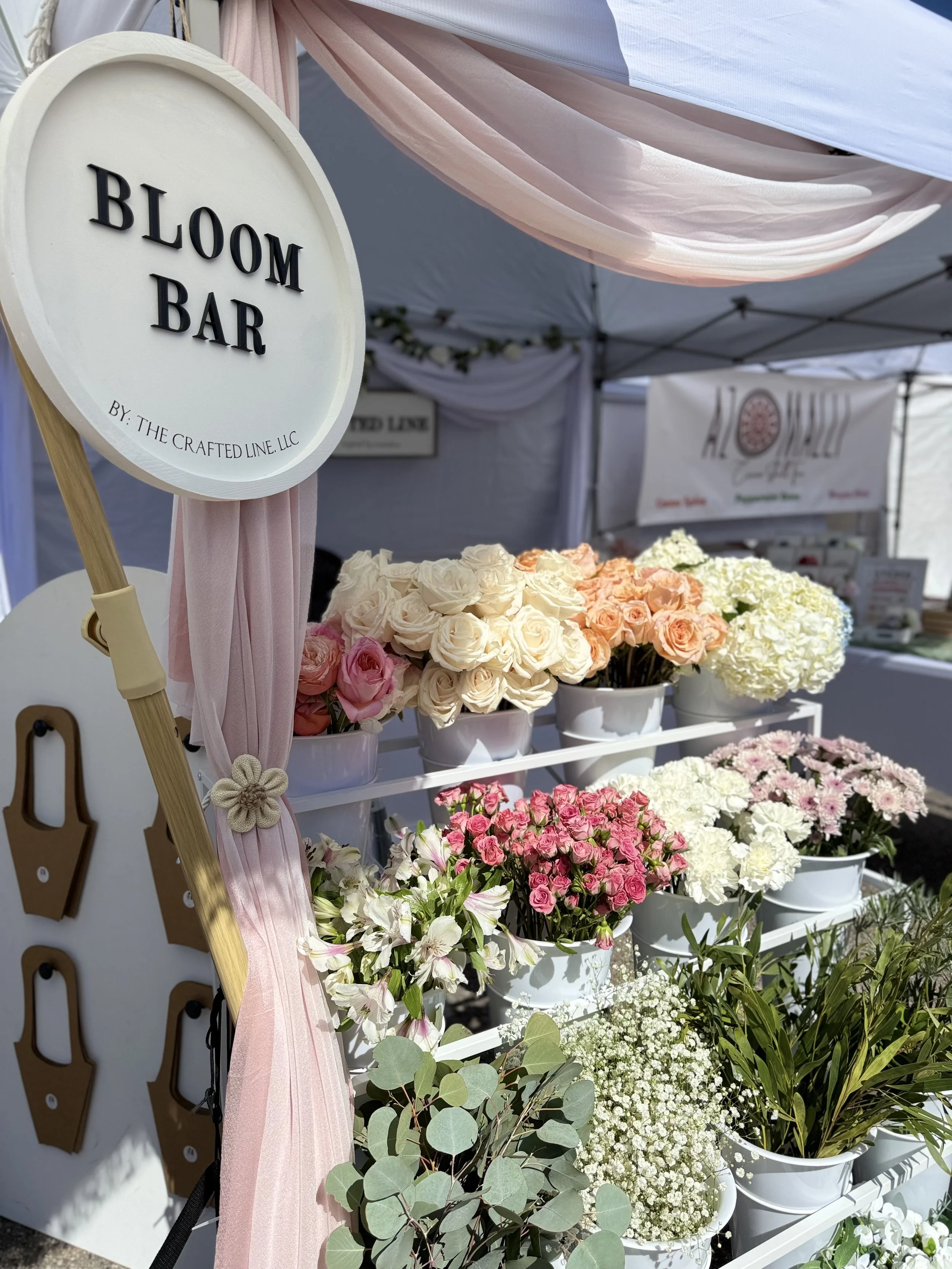 White bloom bar shelves with round signage under a tent at a Colorado event