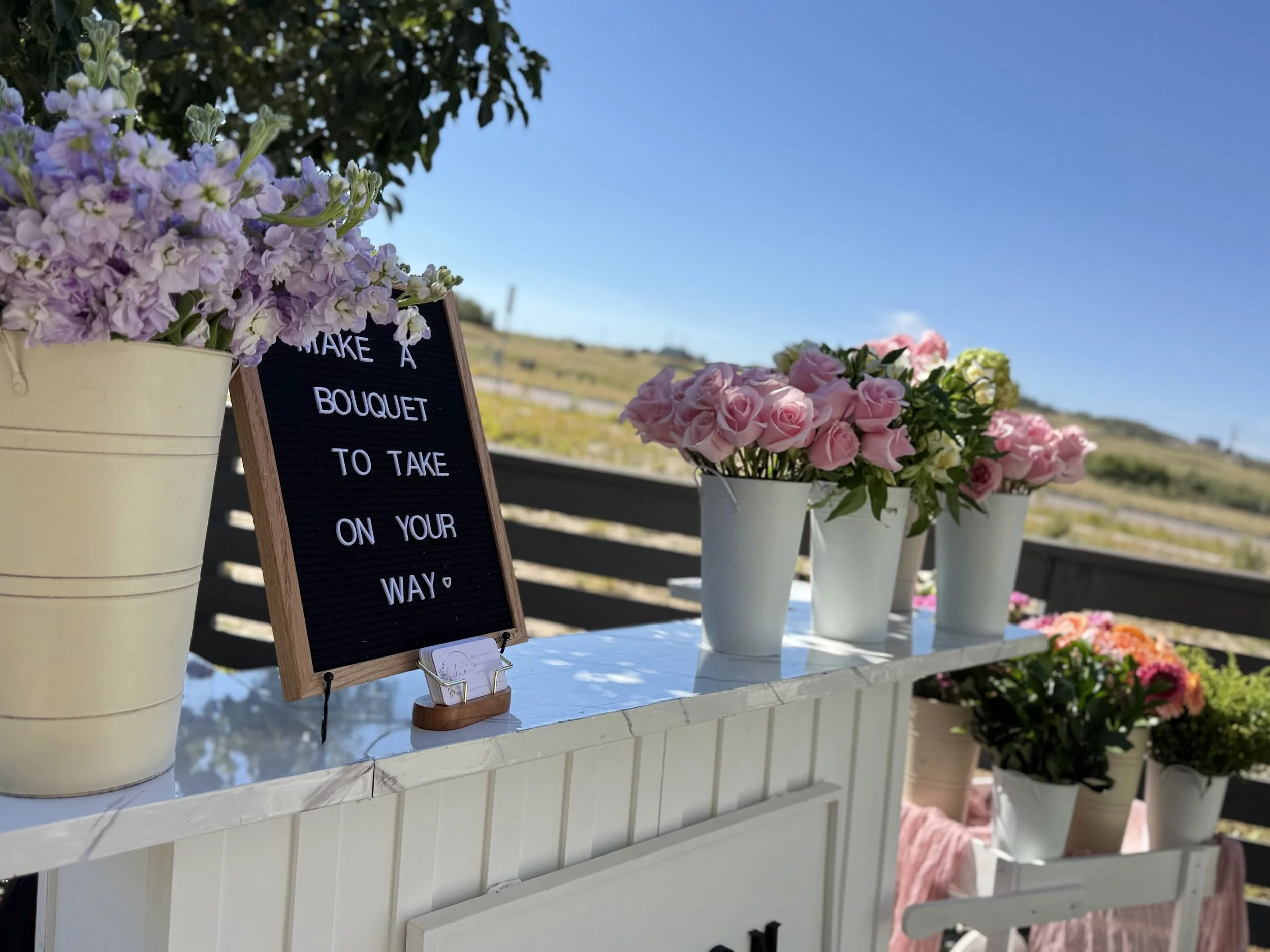 A whimsical white floral cart styled with pastel blooms and vases. A charming add‑on for outdoor events, photo moments, or build‑your‑own‑bouquet stations.