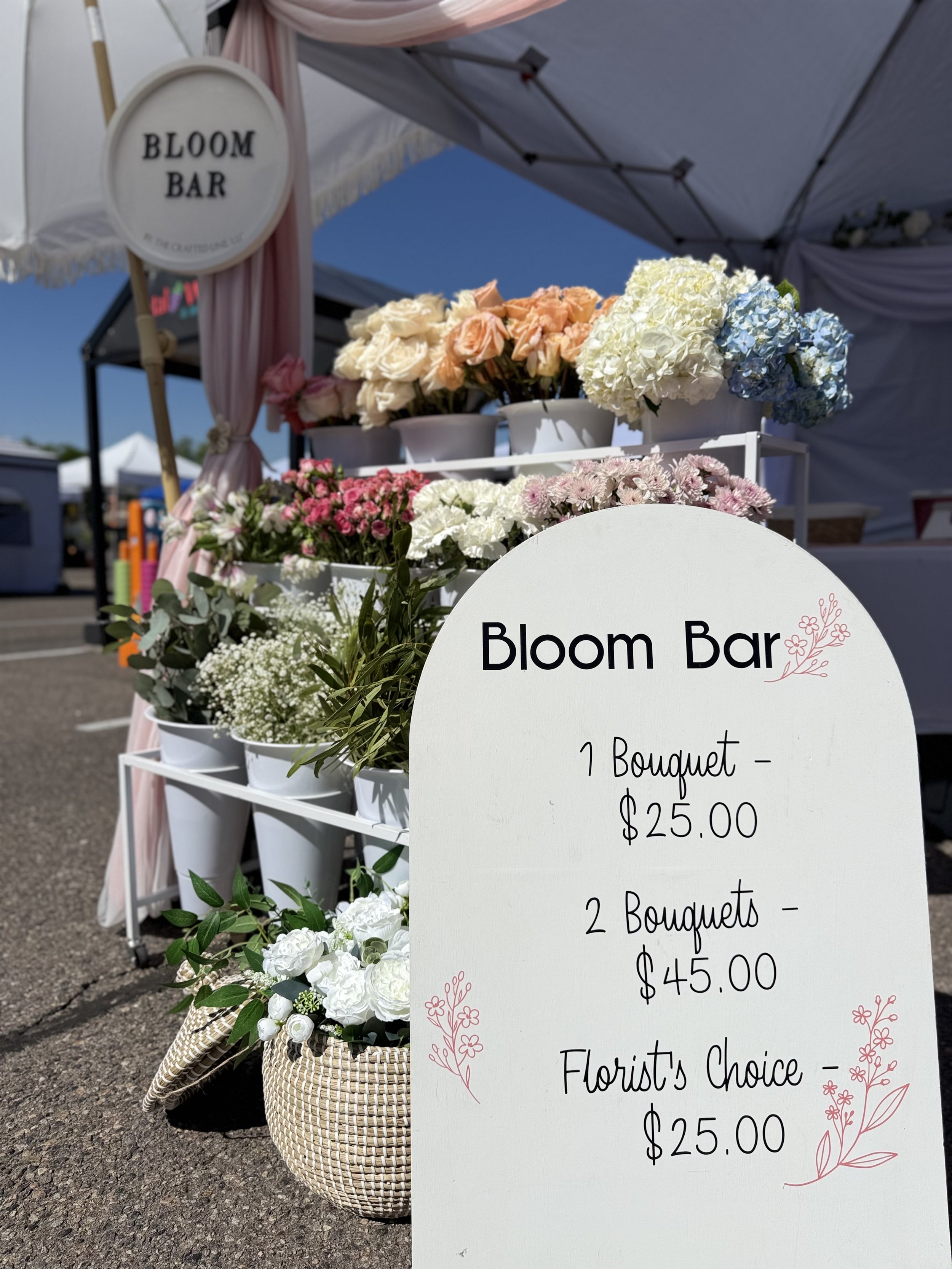 Arched bloom bar sign with pricing beside white flower buckets at a Colorado pop-up