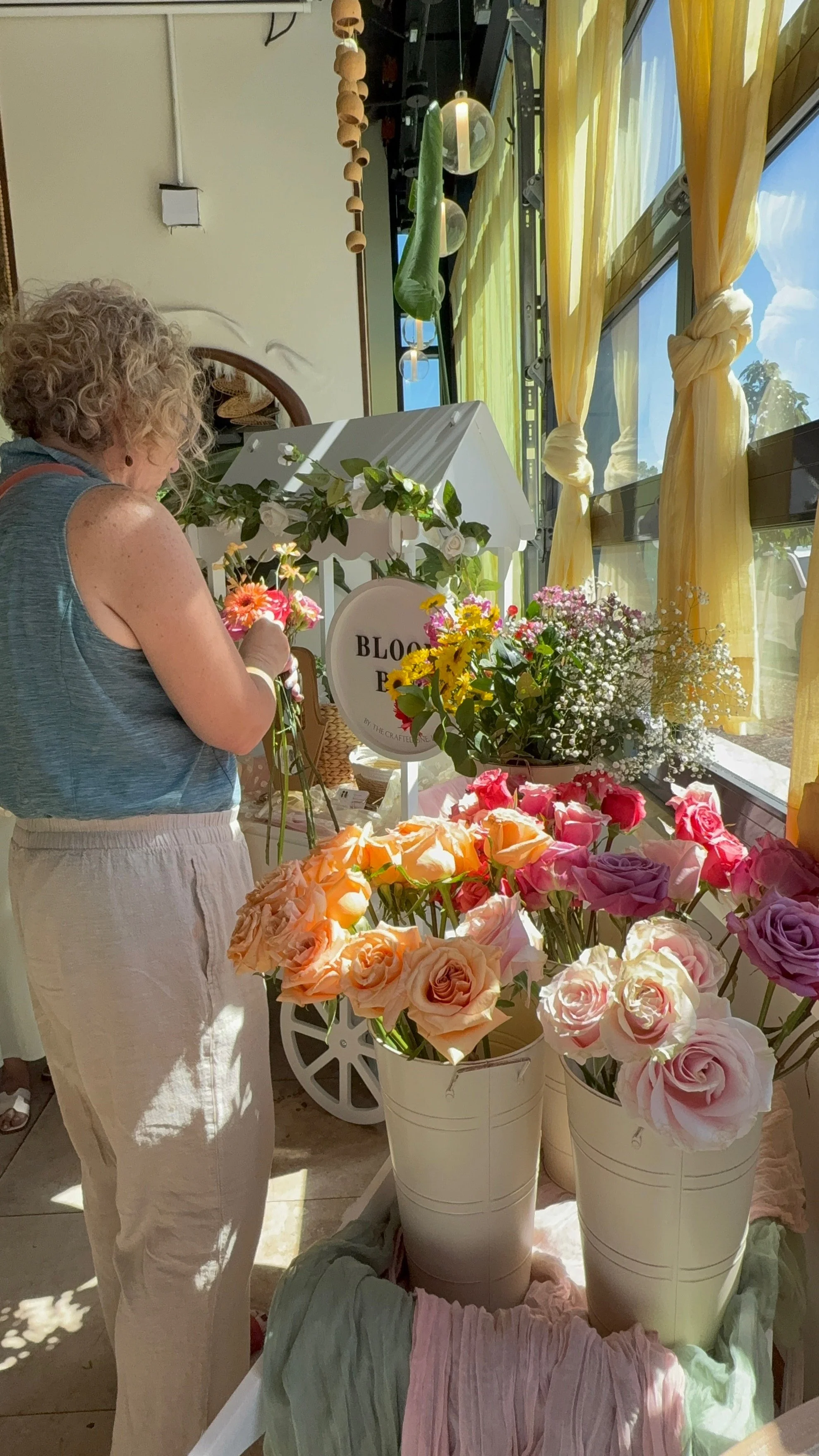 A guest in a blue top arranging her bouquet at the bar, buckets of fresh stems in front of her.