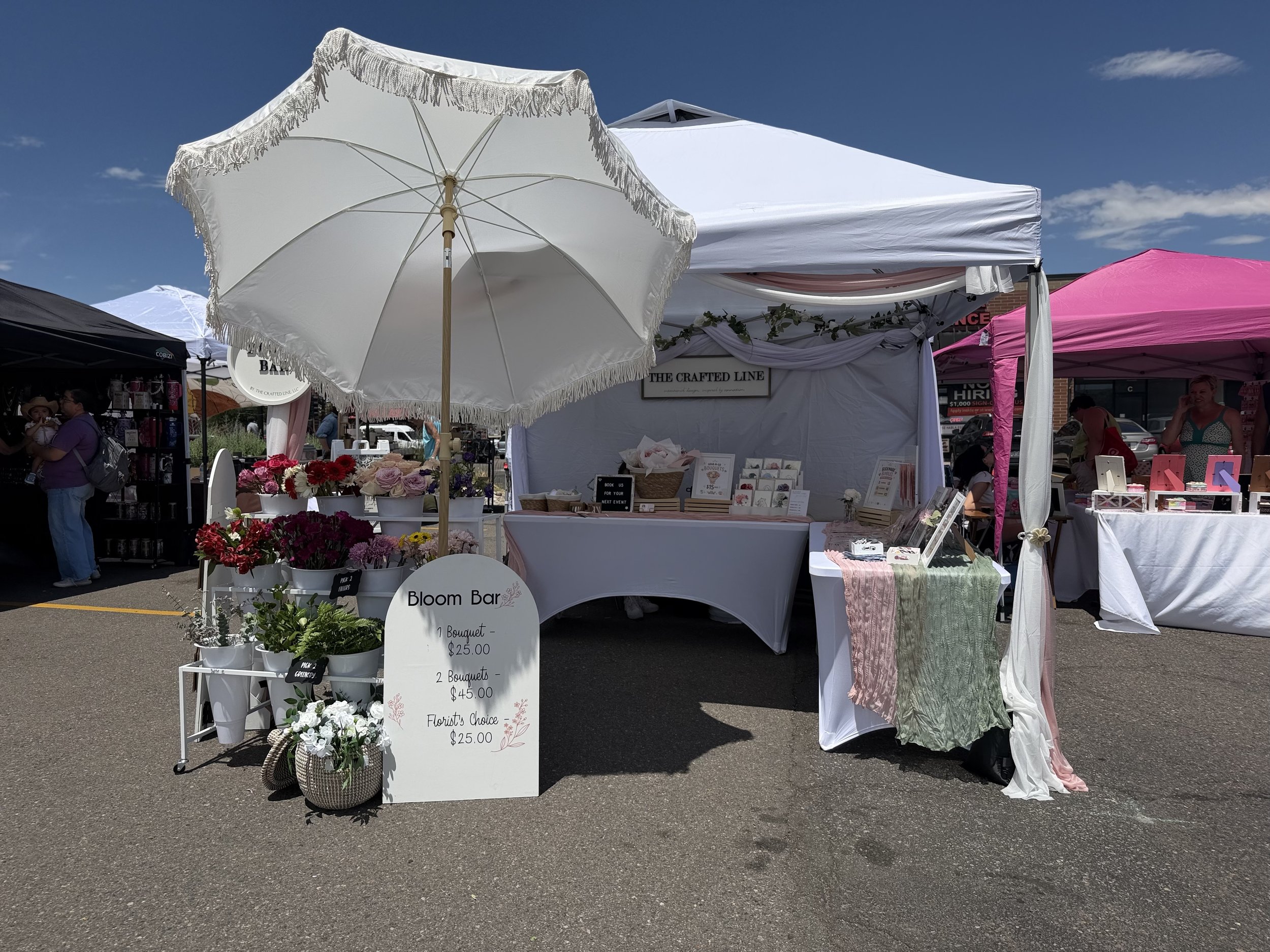 White market tent bloom bar setup with parasol at an outdoor Colorado event