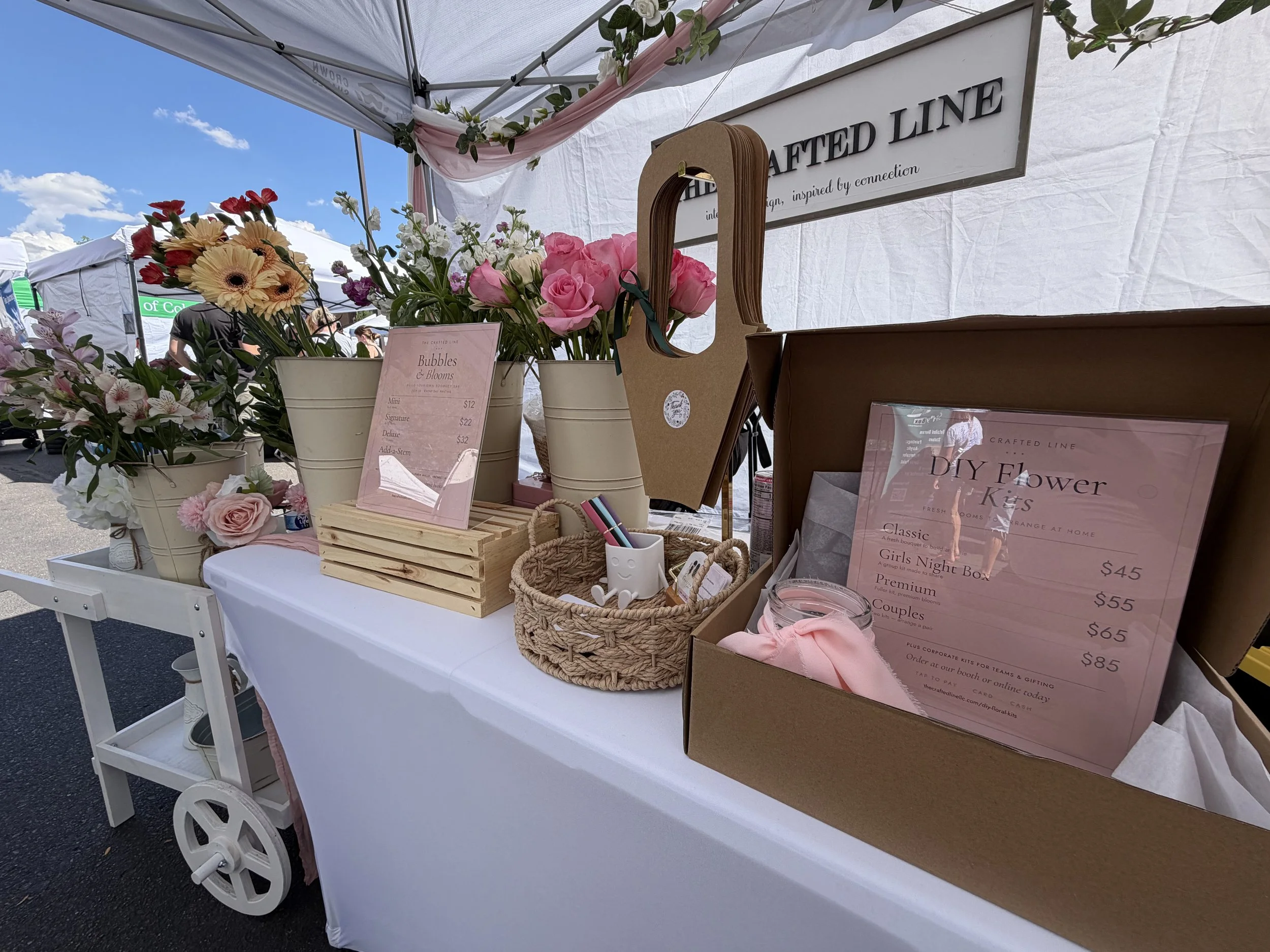 A curated spread of pastel cards, envelopes, and framed pieces arranged with florals for an inviting craft‑fair aesthetic.