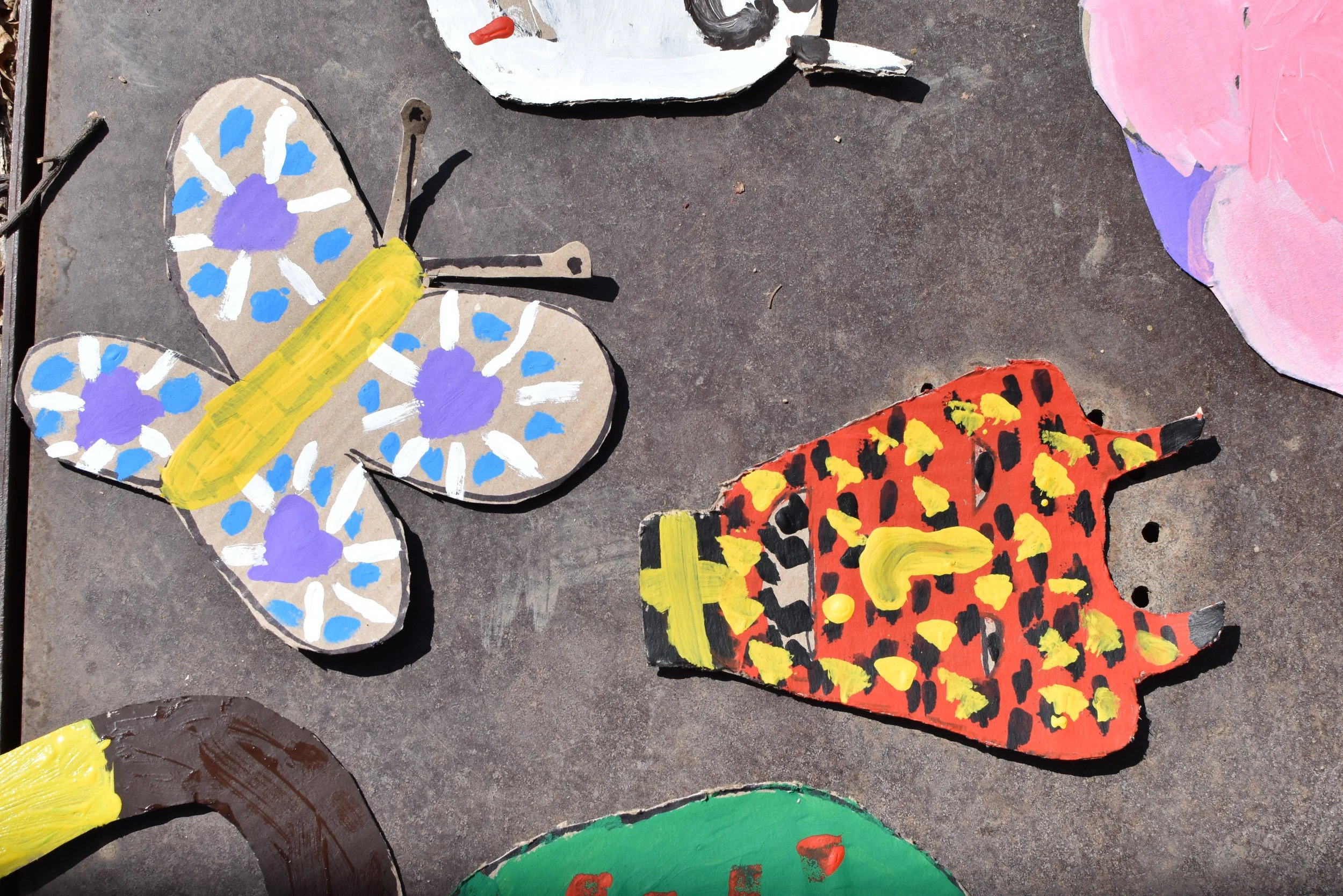 figuras de mariposas y letras pintadas con acrílico en papel reciclado, colocadas sobre una superficie de concreto.
