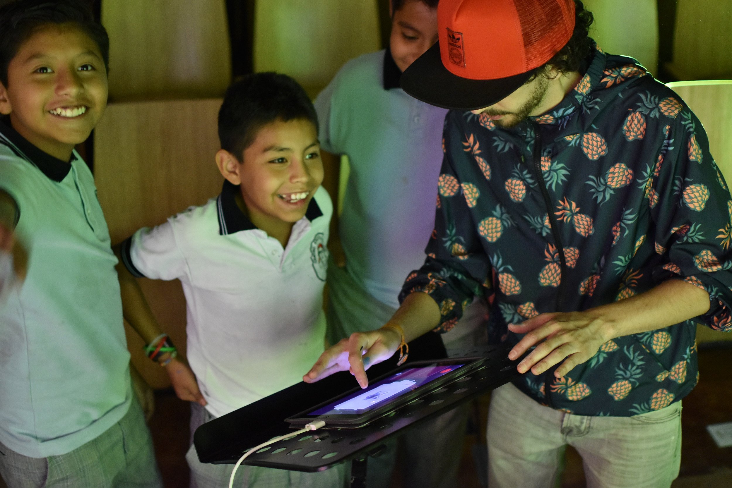 Niños y un adulto interactuando con una tableta en un ambiente interior.