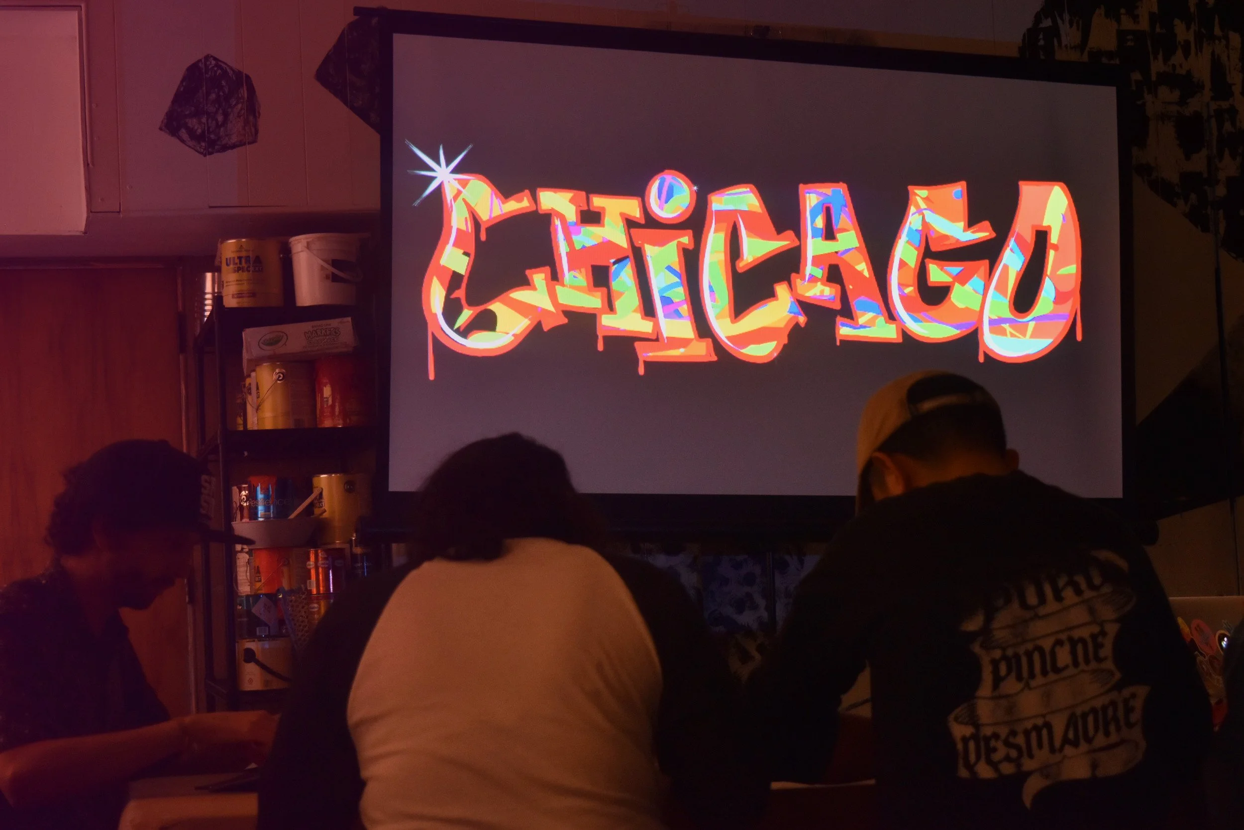 Pantalla que dice 'El Clan' en letras coloridas en un ambiente oscuro con varias personas observando.