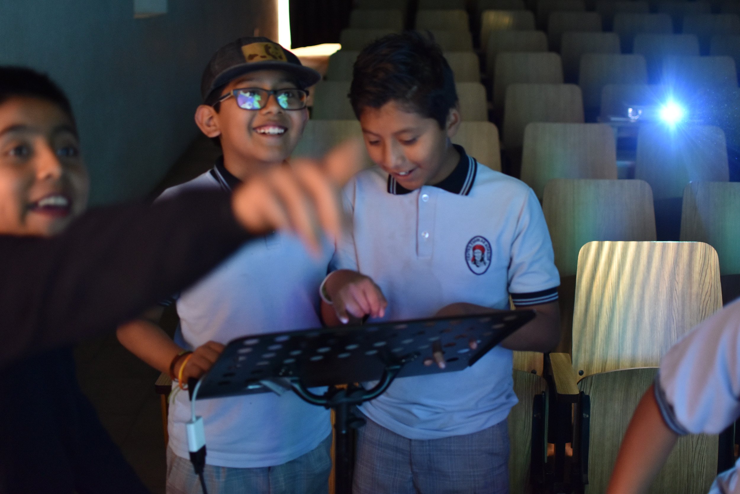Niños en un cine viendo una película, uno de ellos con gafas y sonriente, y otro mirando atentamente.