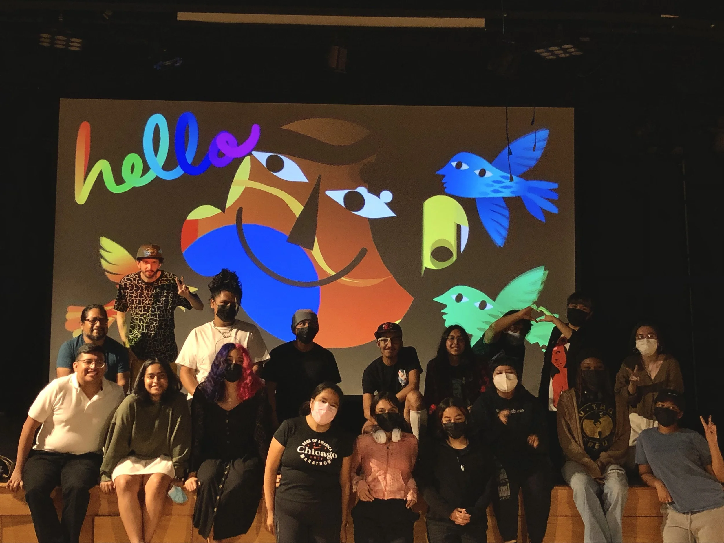Grupo de personas en un evento frente a una pantalla con ilustraciones de aves y el texto 'hello'.