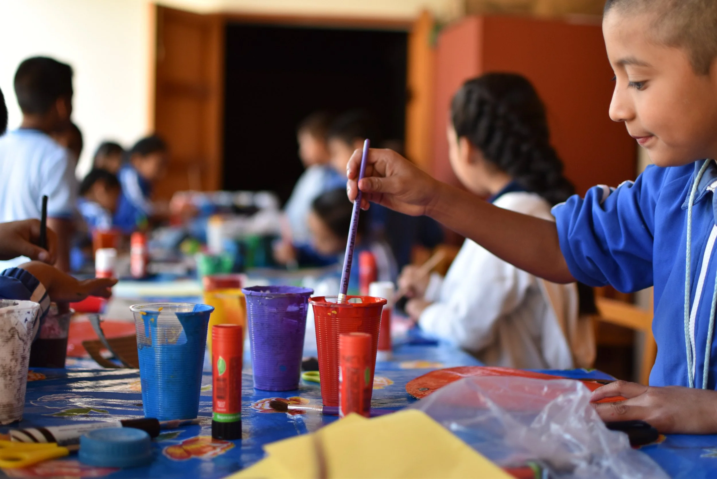 Niños en una clase de arte pintando con colores y pinceles.