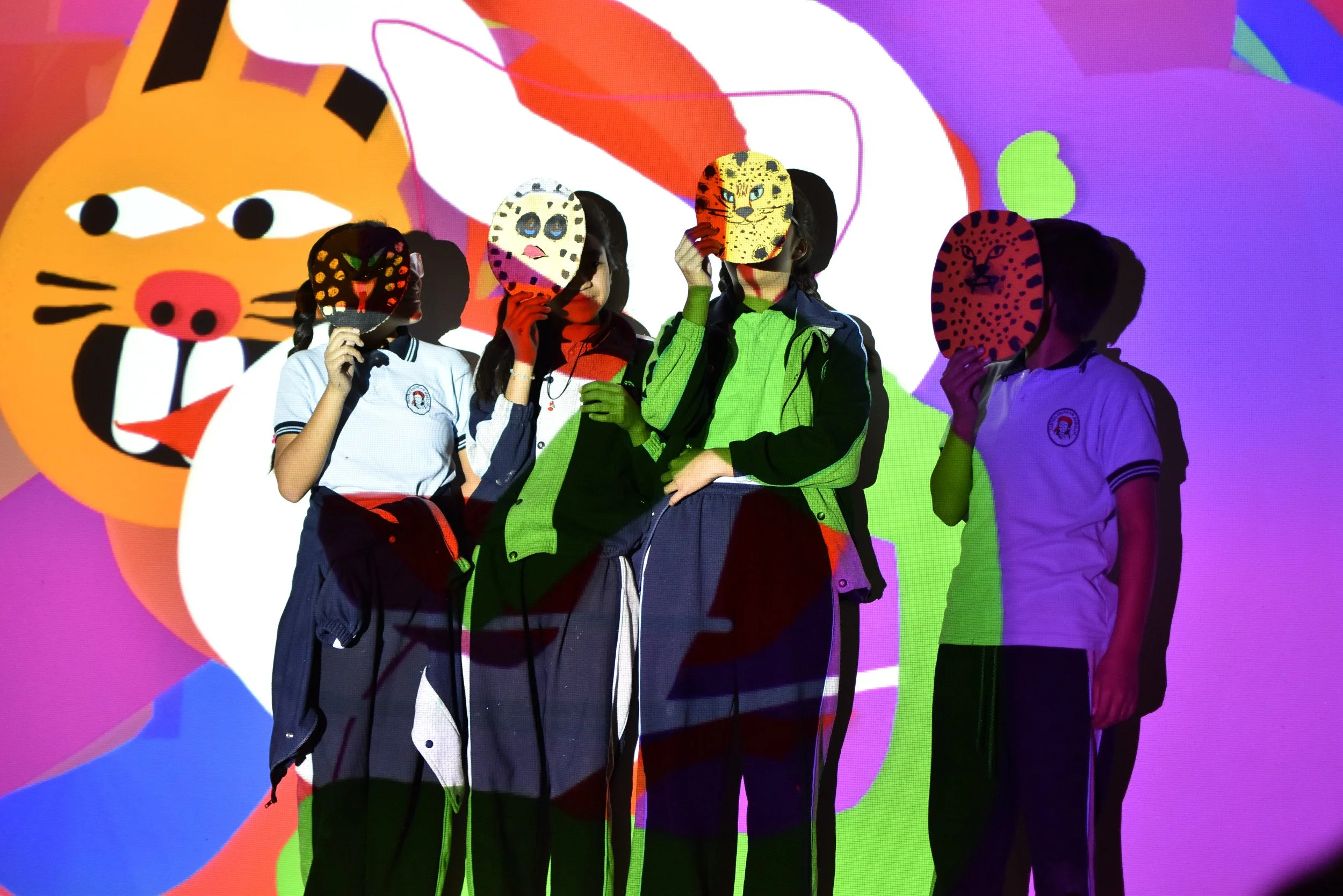 Cuatro personas con máscaras de animales frente a una pantalla con ilustraciones de animales y colores vivos.