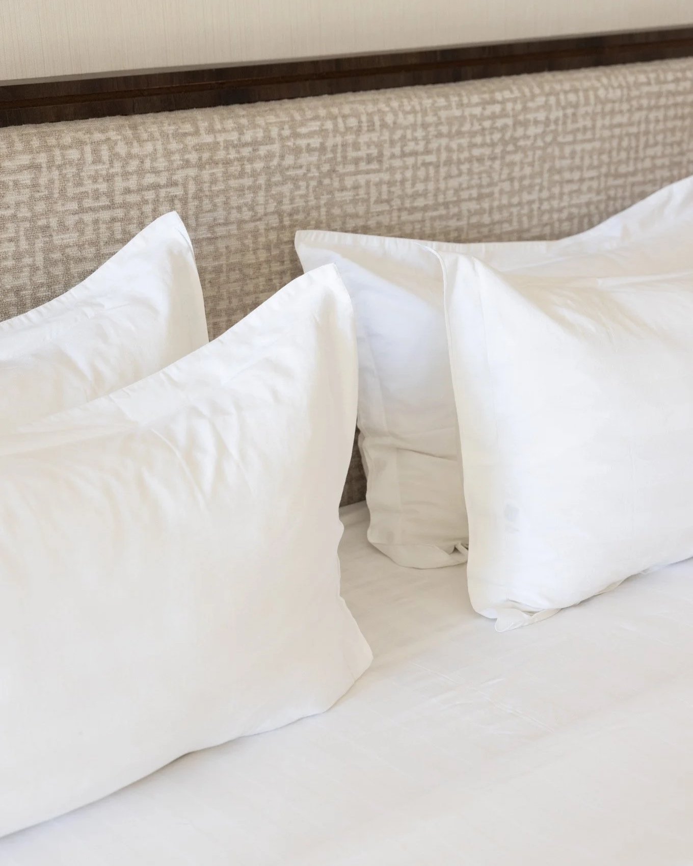 Close-up of a bed with white pillows and a beige textured headboard.