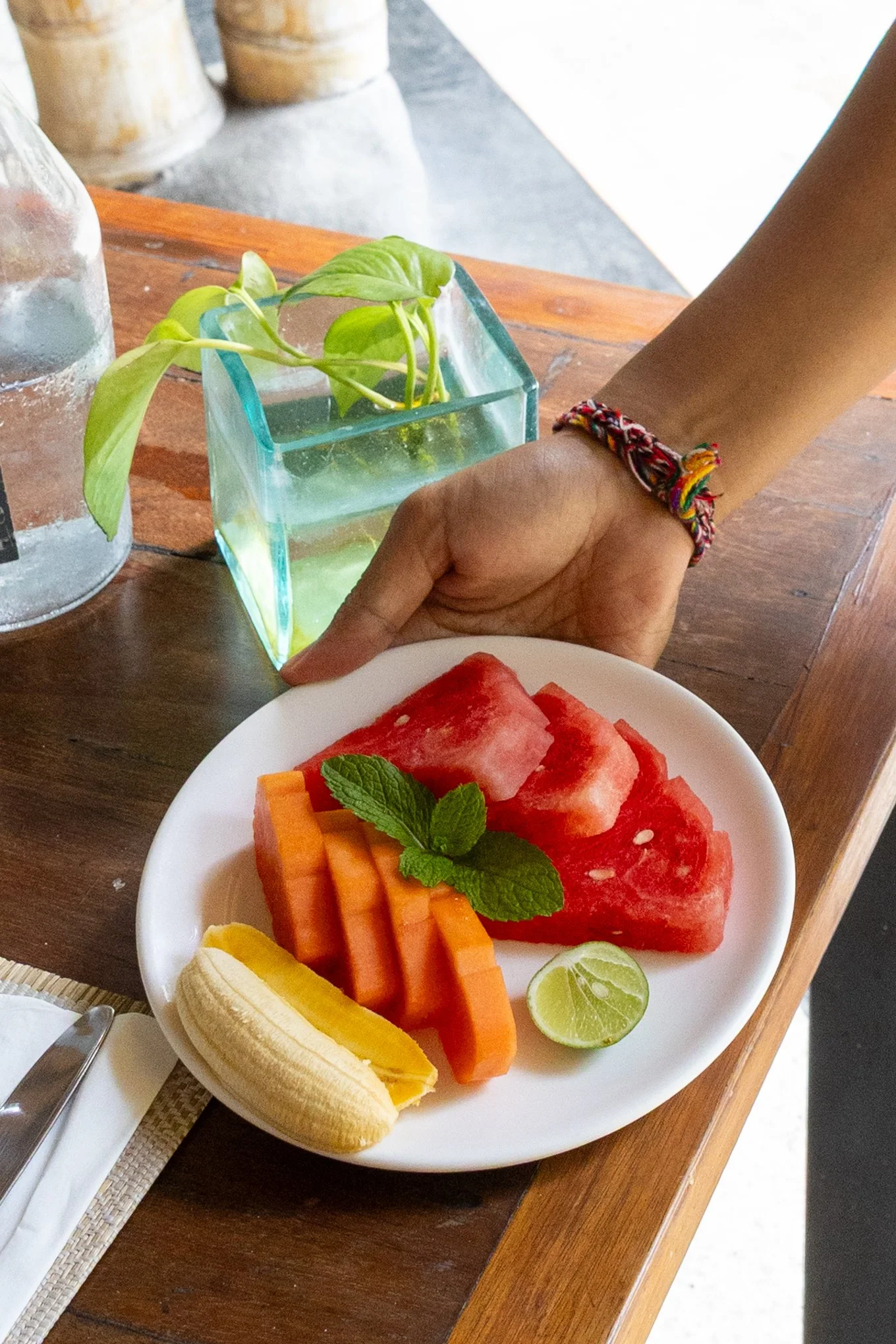 Plate of sliced watermelon, cantaloupe, papaya, banana, lemon, and lime served with fresh mint leaves.