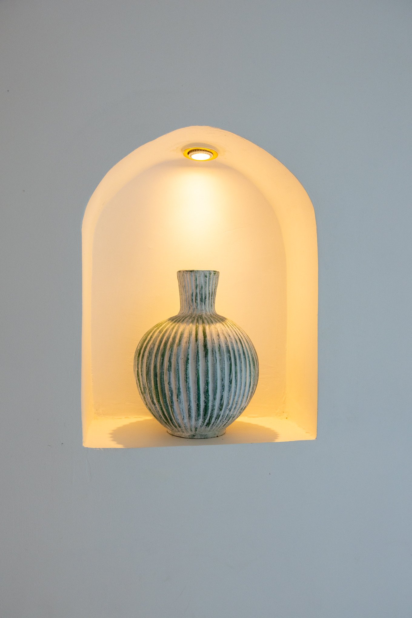 A striped ceramic vase placed within a lit alcove in the wall, casting warm light around it.
