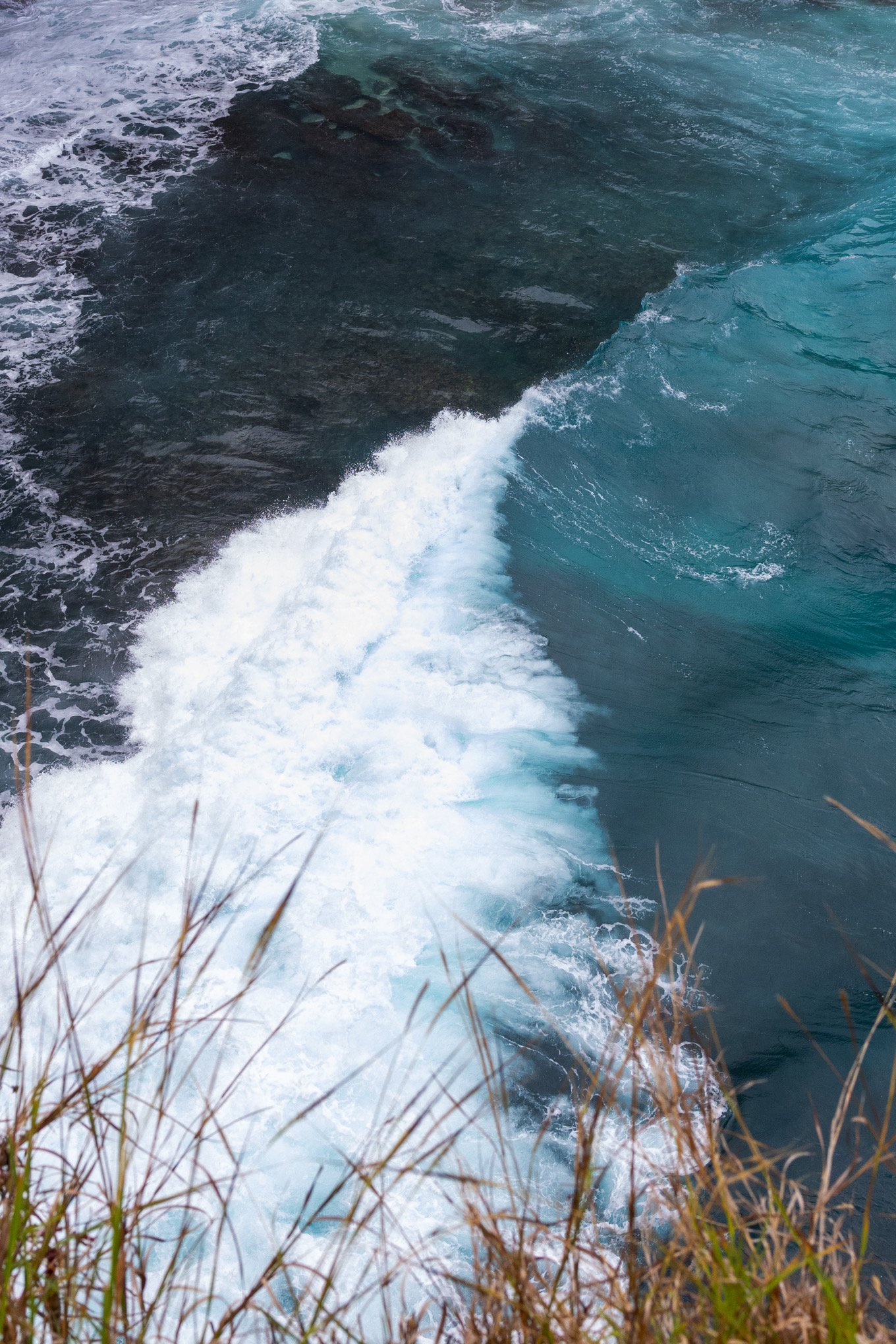 Streams of water with rocks visible underwater, surrounded by some brown grass in the foreground.