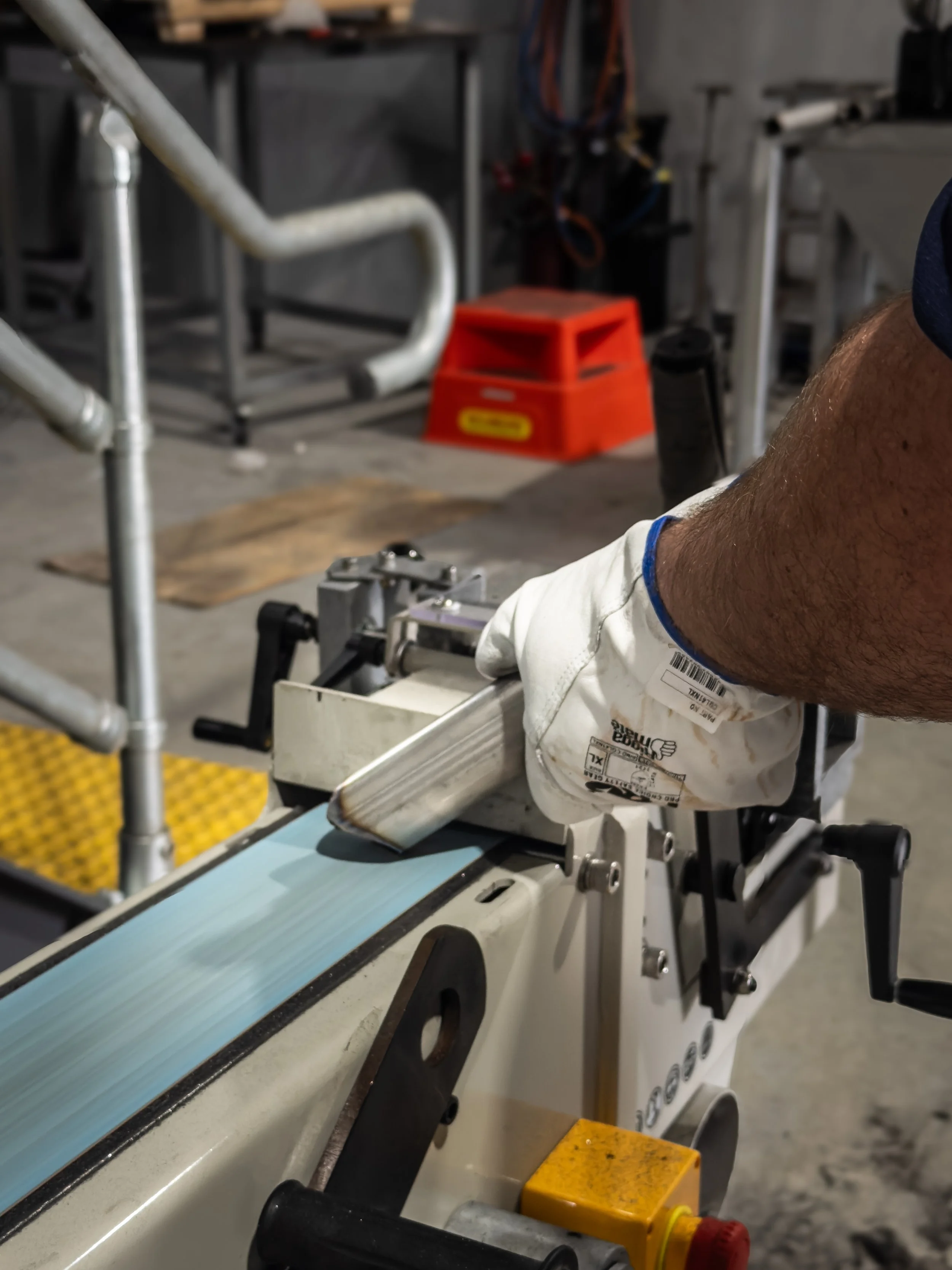 Close-up of a worker operating industrial machinery in a workshop, with focus on the worker's arm and machinery controls.