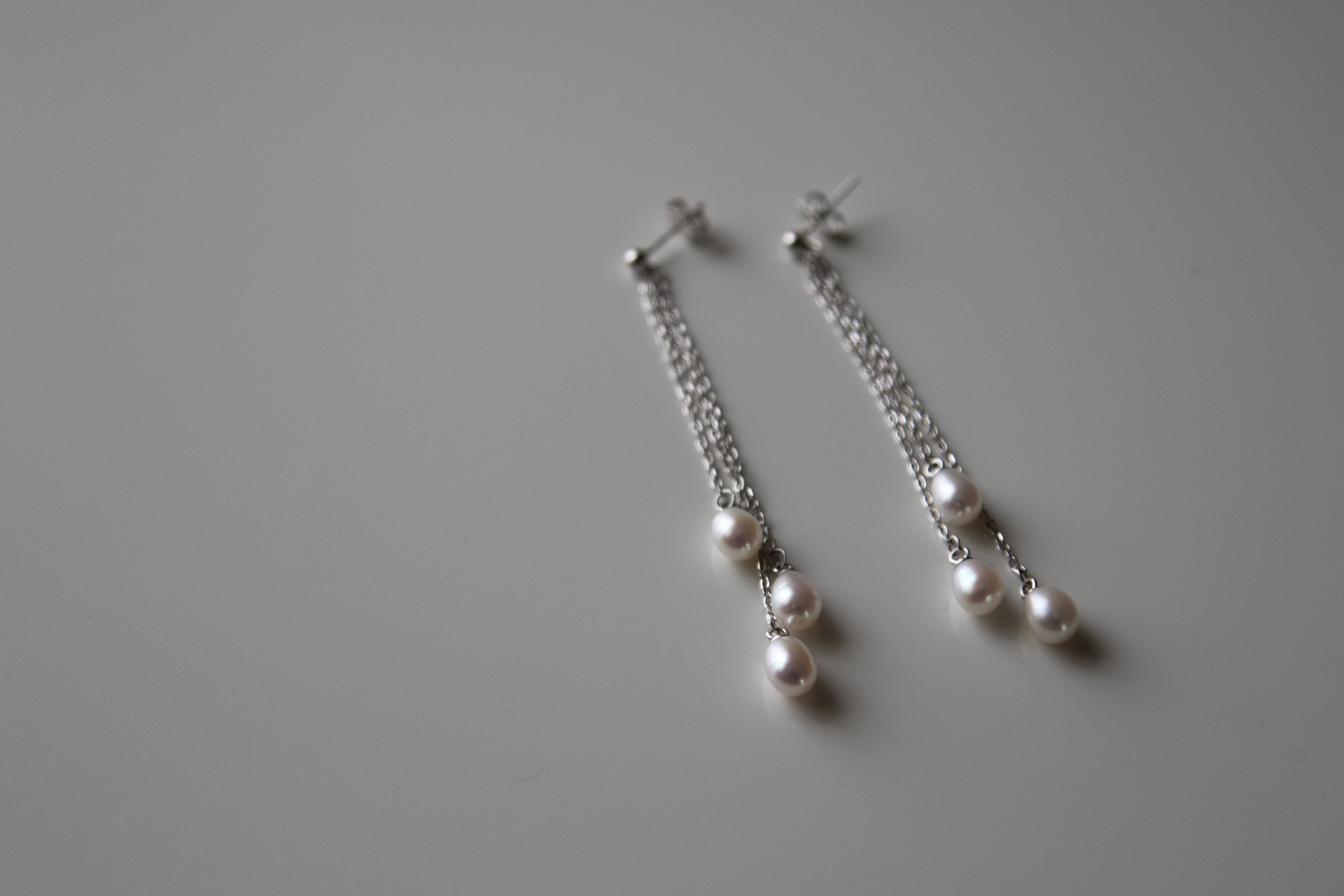 Pair of pearl and silver chain earrings on a light gray surface.