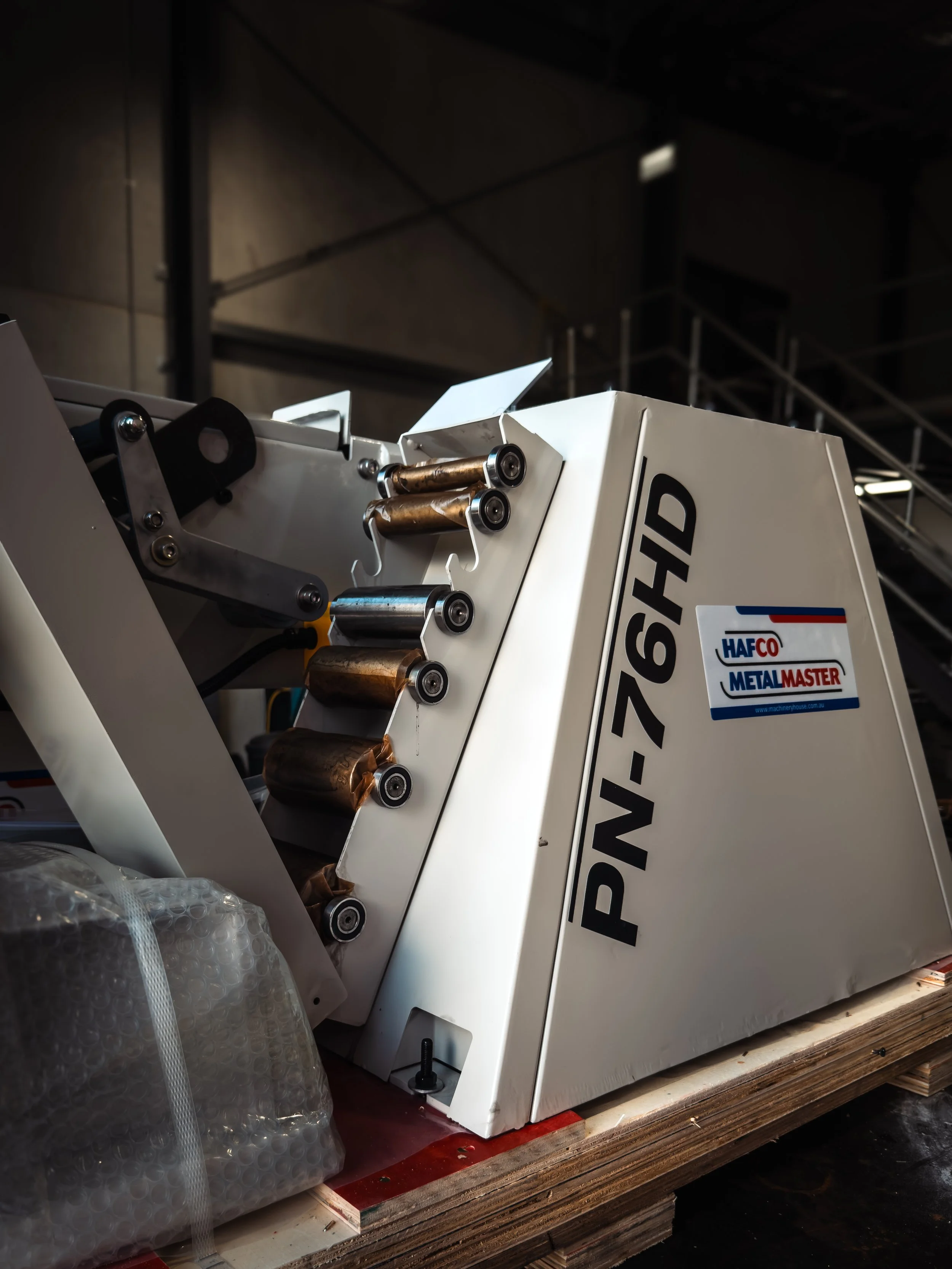 Close-up of industrial machinery with white panels, rollers, and bolts in a workshop. 