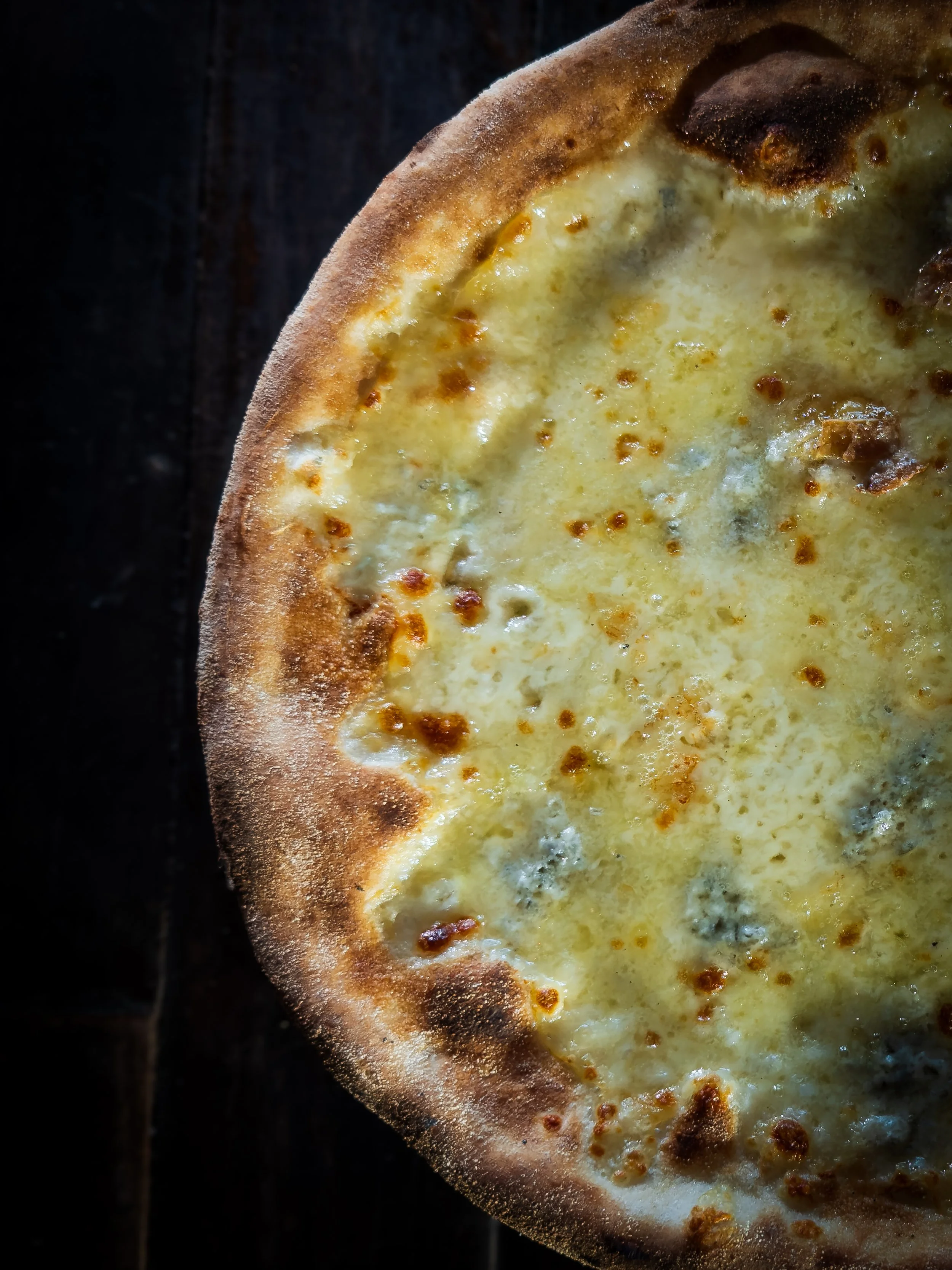 Close-up of a cheese pizza with a golden-brown crust on a dark surface.