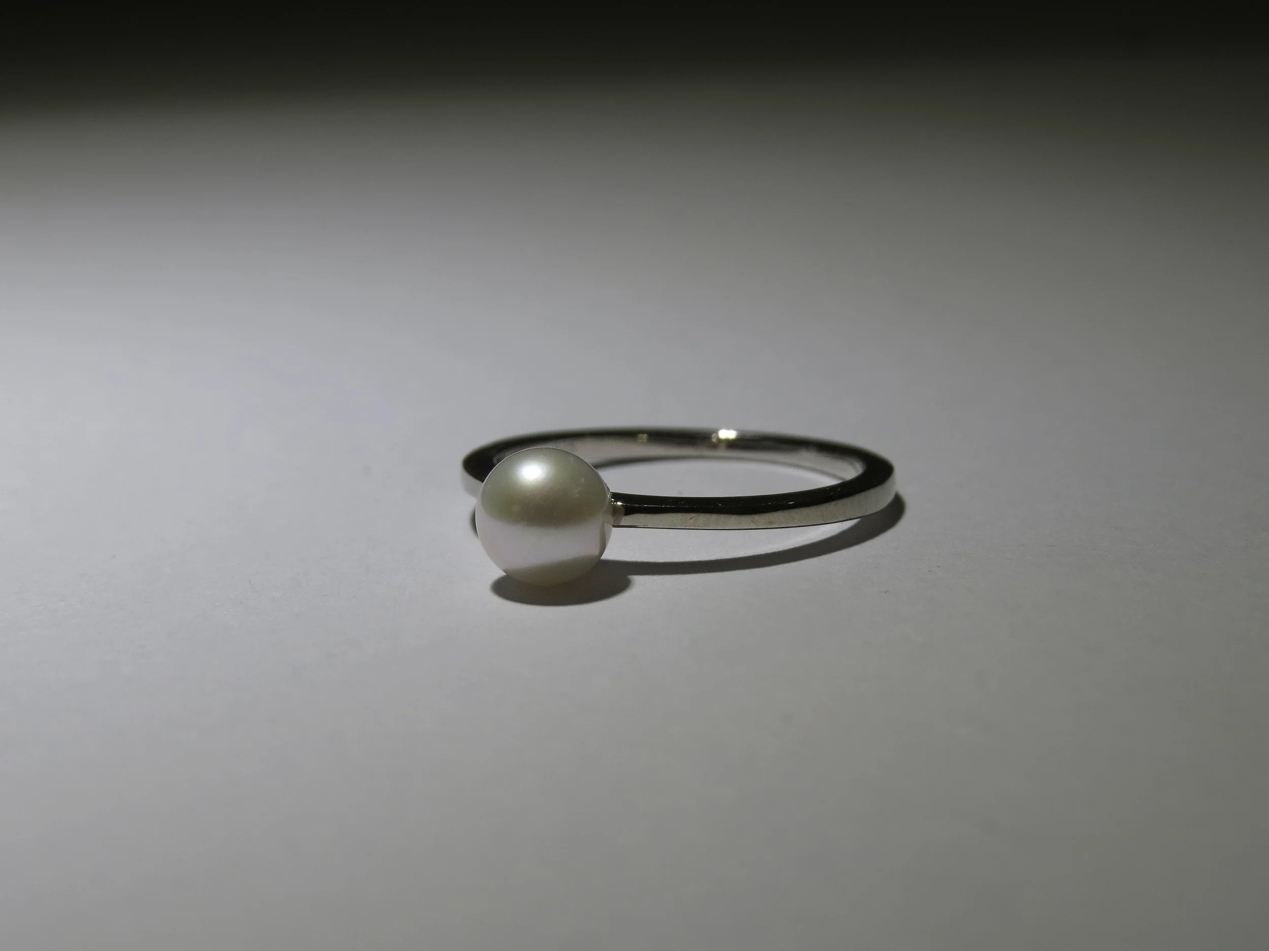 A silver ring with a large white pearl placed on a plain white surface.