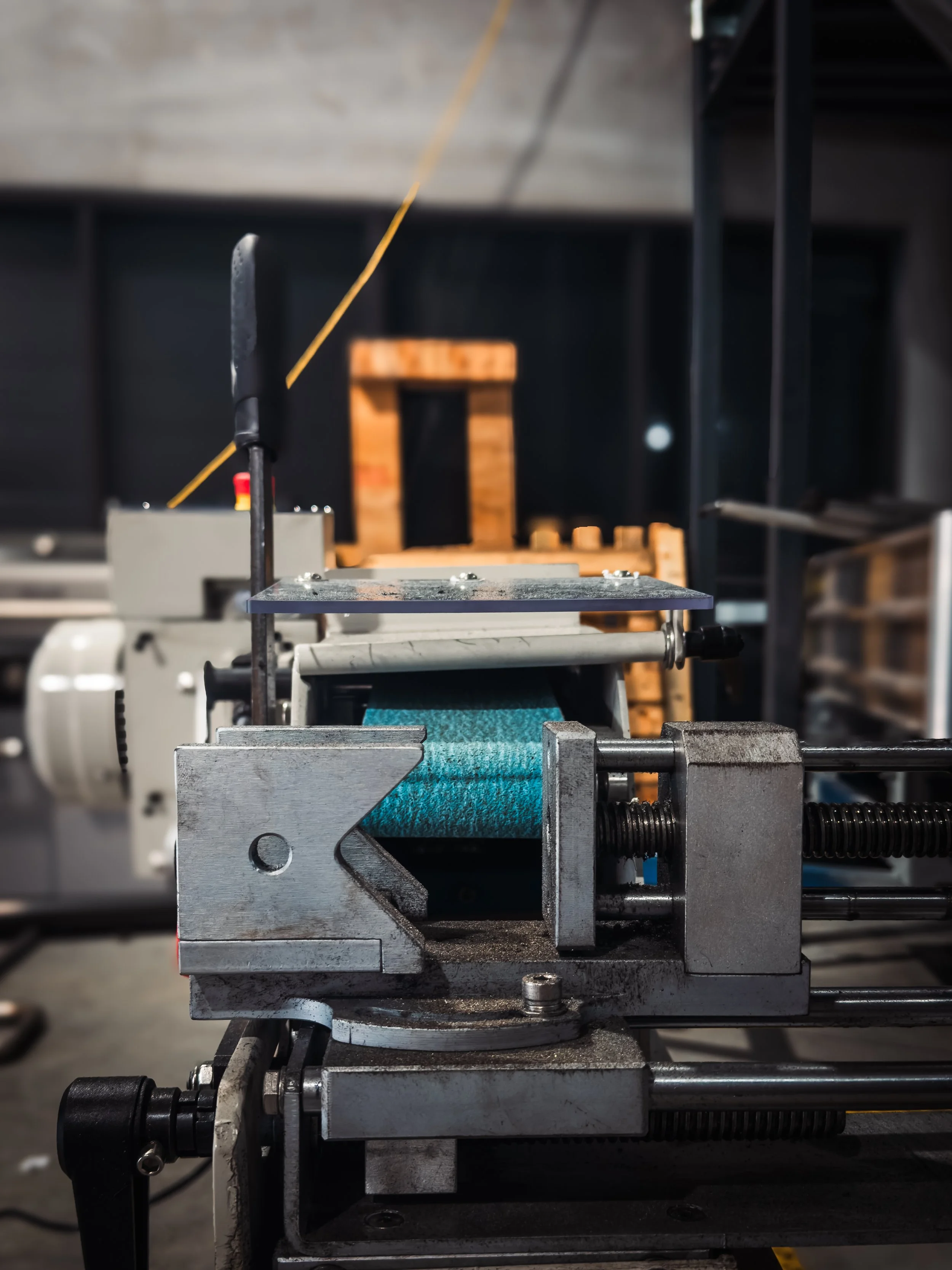 Close-up of industrial machinery with metal components, bolts, and a blue belt, in a workshop or manufacturing setting.