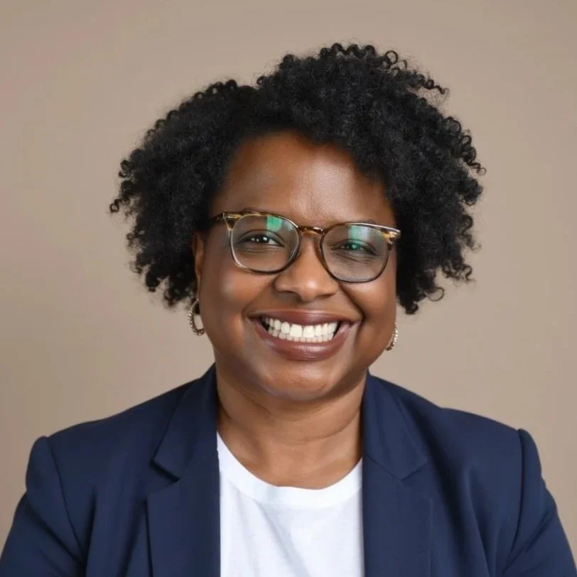 Dr. Orletta Caldwell with curly black hair wearing glasses, earrings, a navy blazer, and a white shirt, against a neutral background.
