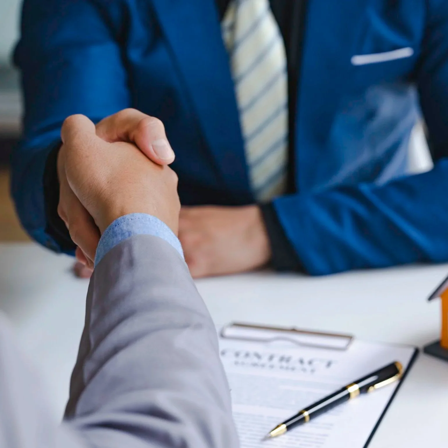 Close-up of two people shaking hands in a professional setting, with office items like a pen and documents on a table.