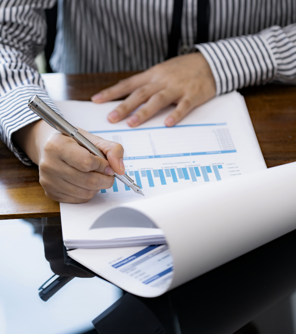 Person in a striped shirt analyzing documents with bar graphs on a wooden table.