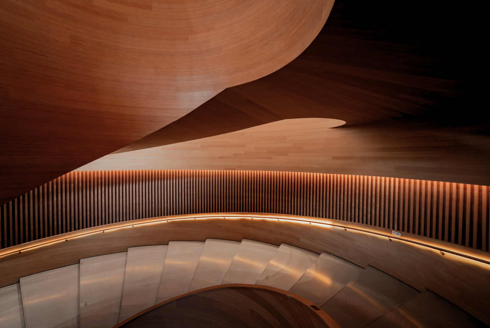 Spiral staircase with wooden and metal design, illuminated with warm lighting, viewed from above.