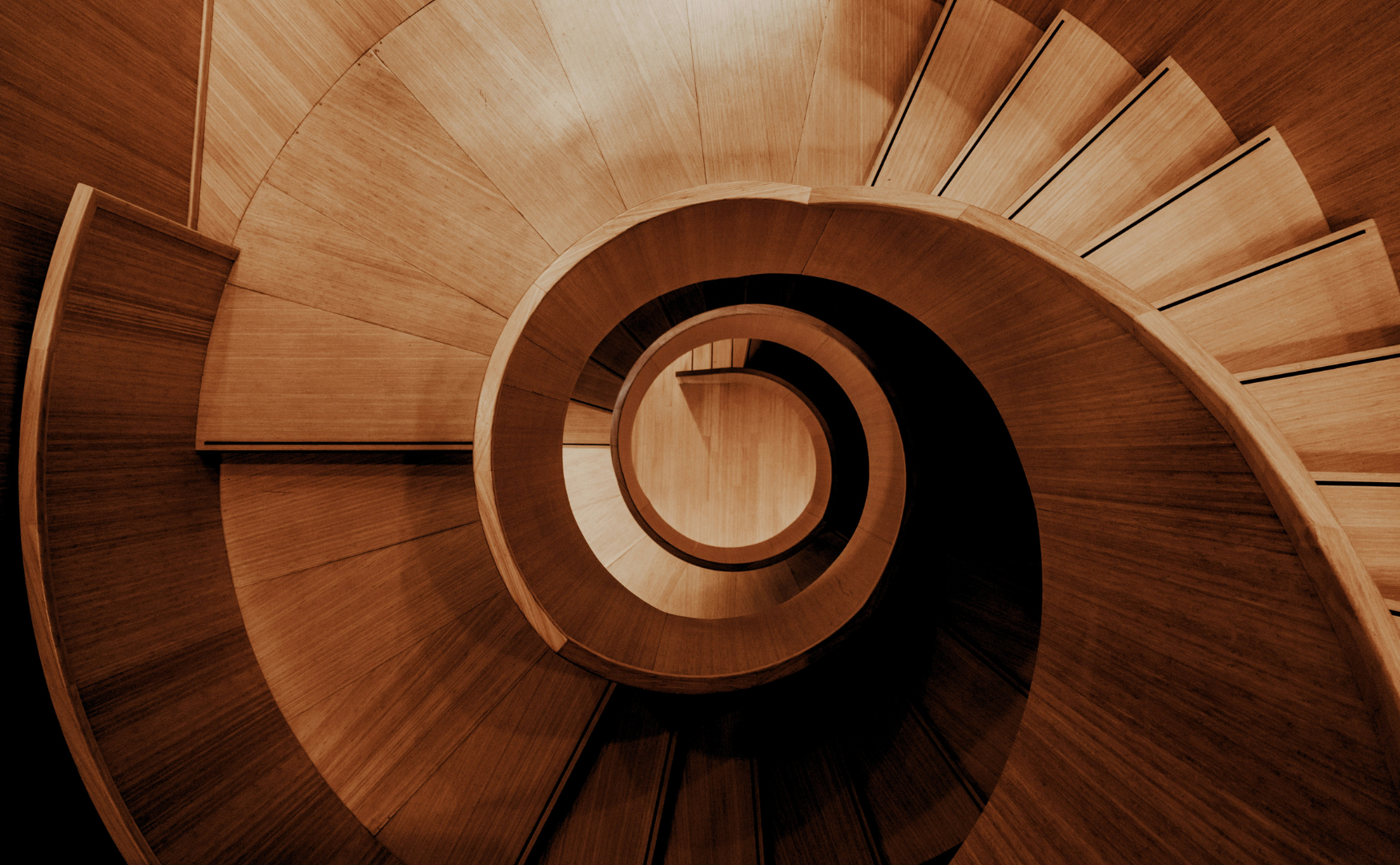 Top-down view of a wooden spiral staircase with curved steps and a rounded handrail.