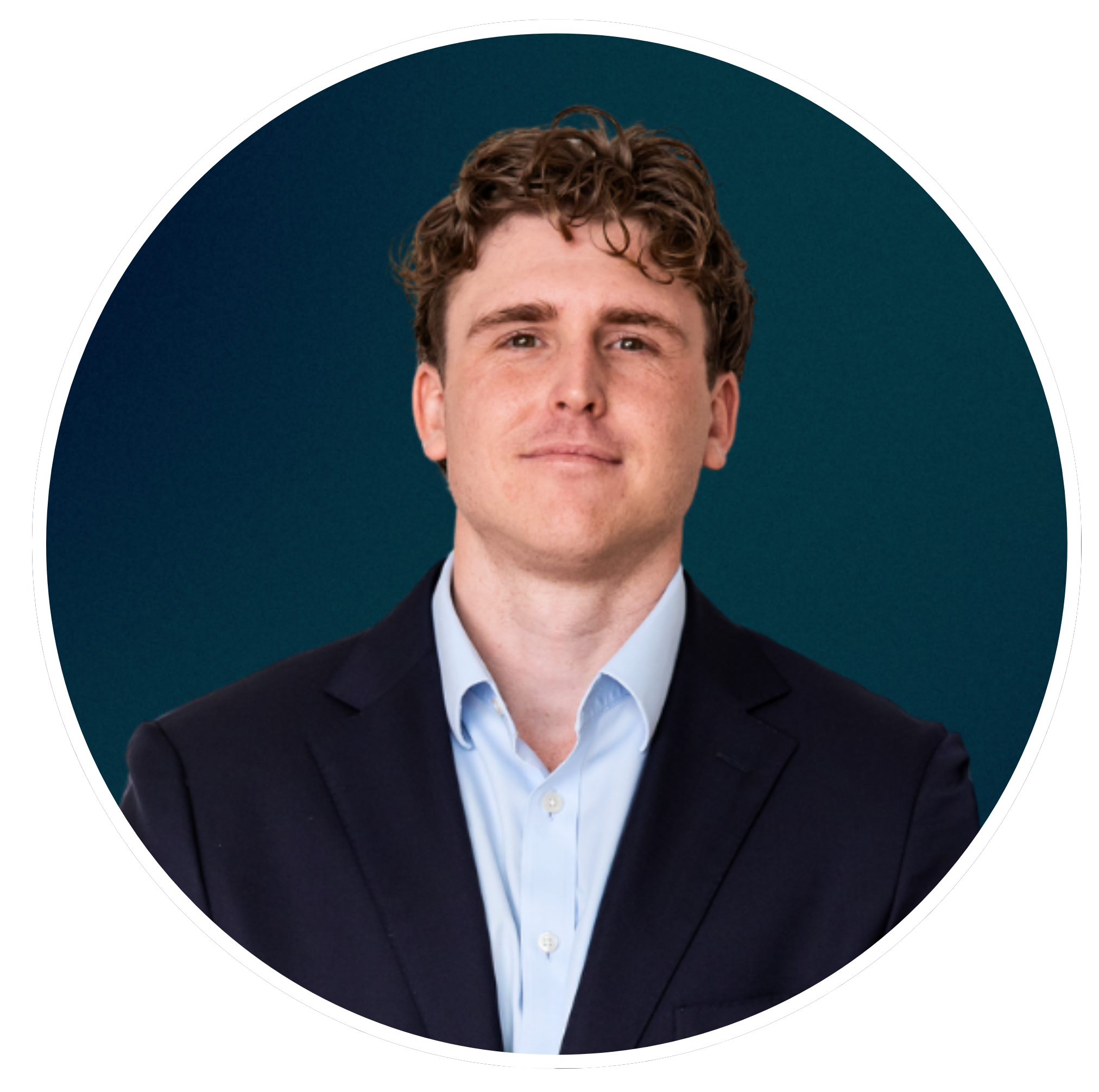 A young man with curly brown hair, wearing a dark suit and light blue shirt, smiling softly against a dark teal background.